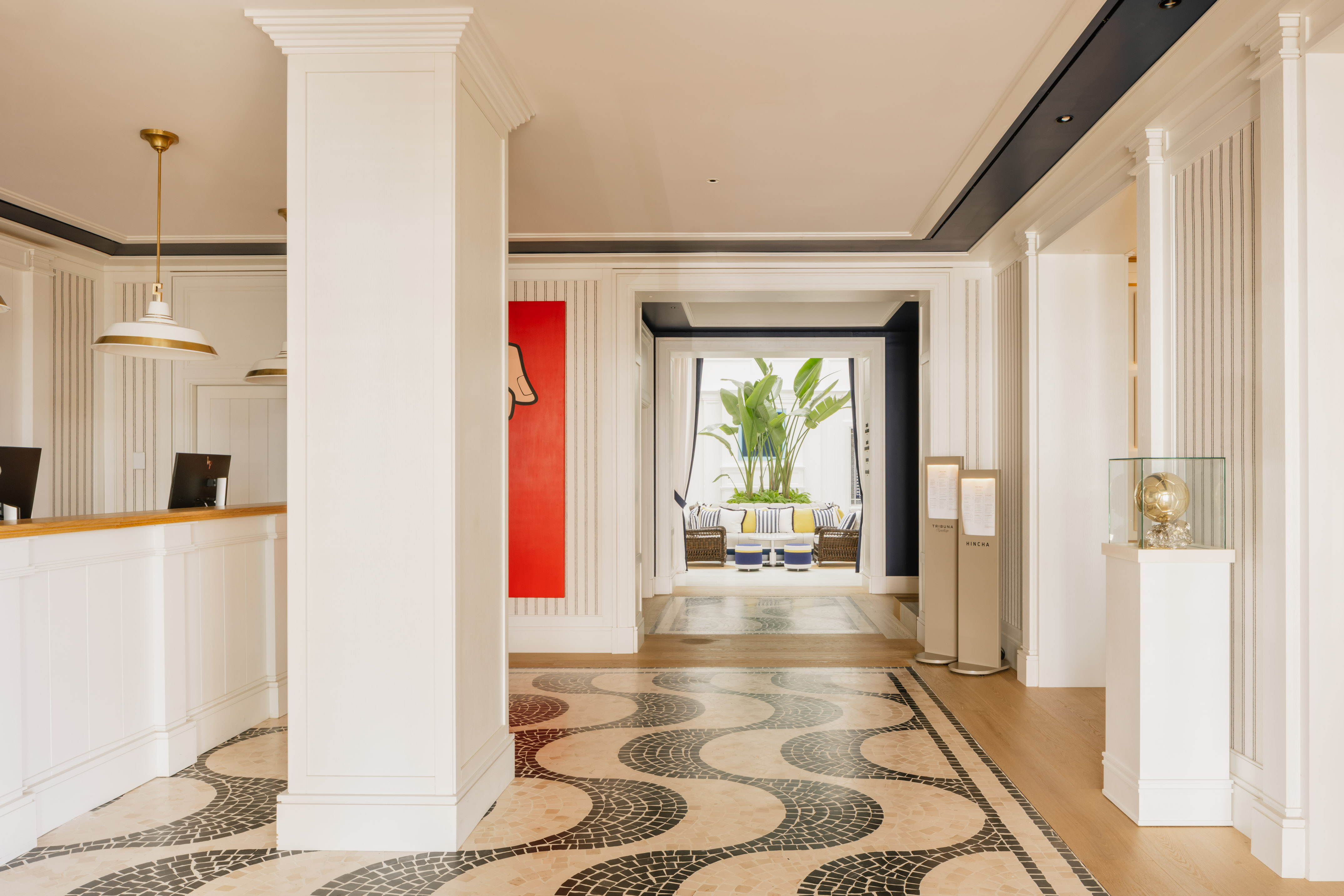 Elegant hotel reception with wavy mosaic floor and lush tropical lounge beyond.