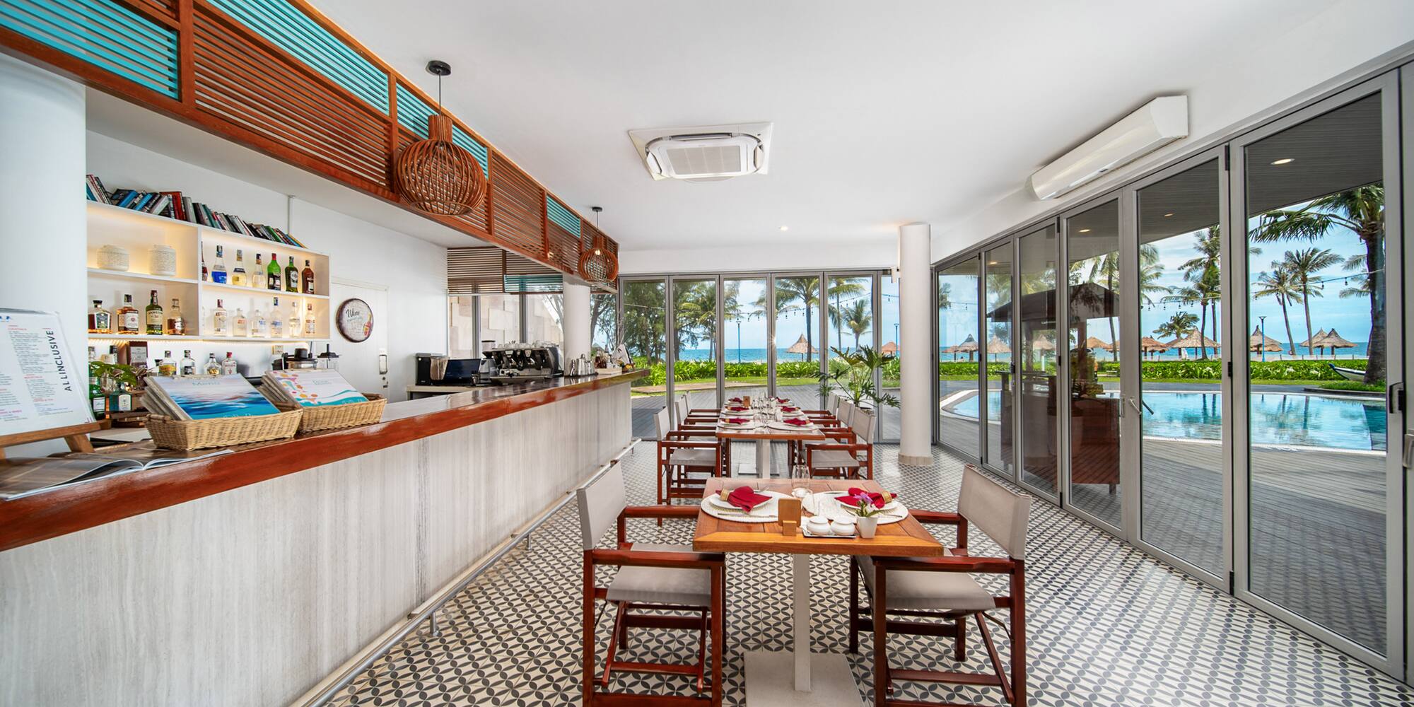Beachfront resort restaurant and bar with set tables and ocean view.