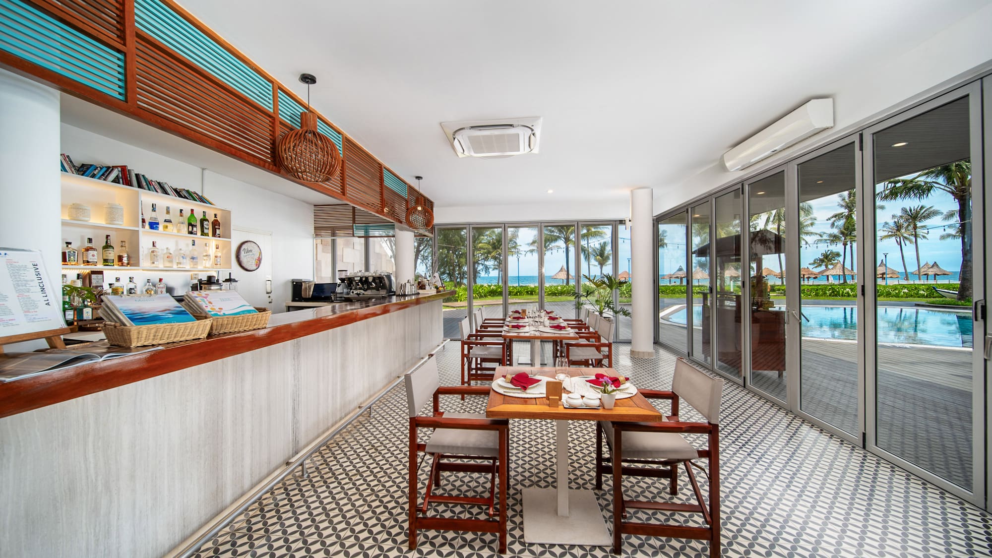Beachfront resort restaurant and bar with set tables and ocean view.