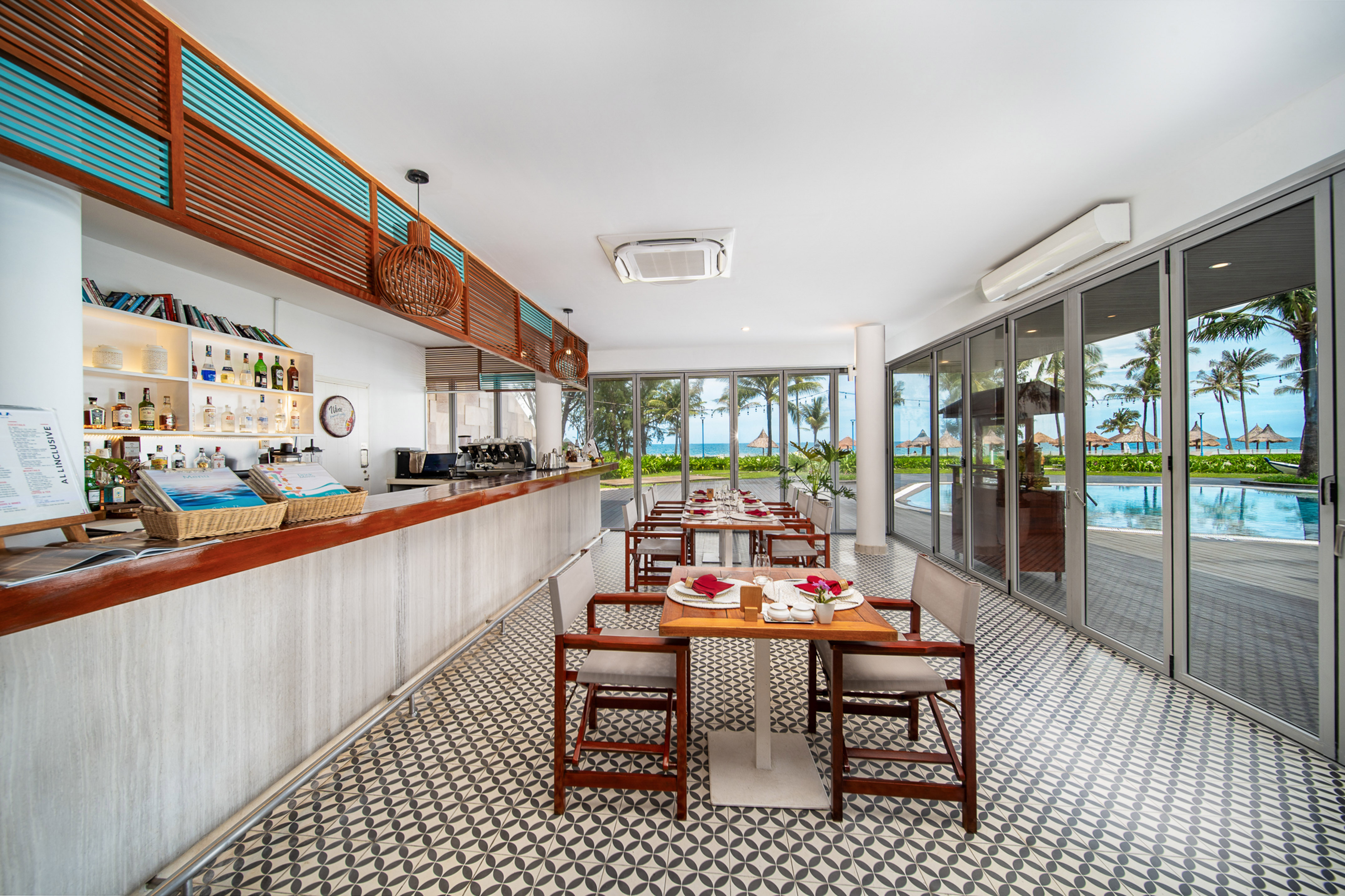 Beachfront resort restaurant and bar with set tables and ocean view.