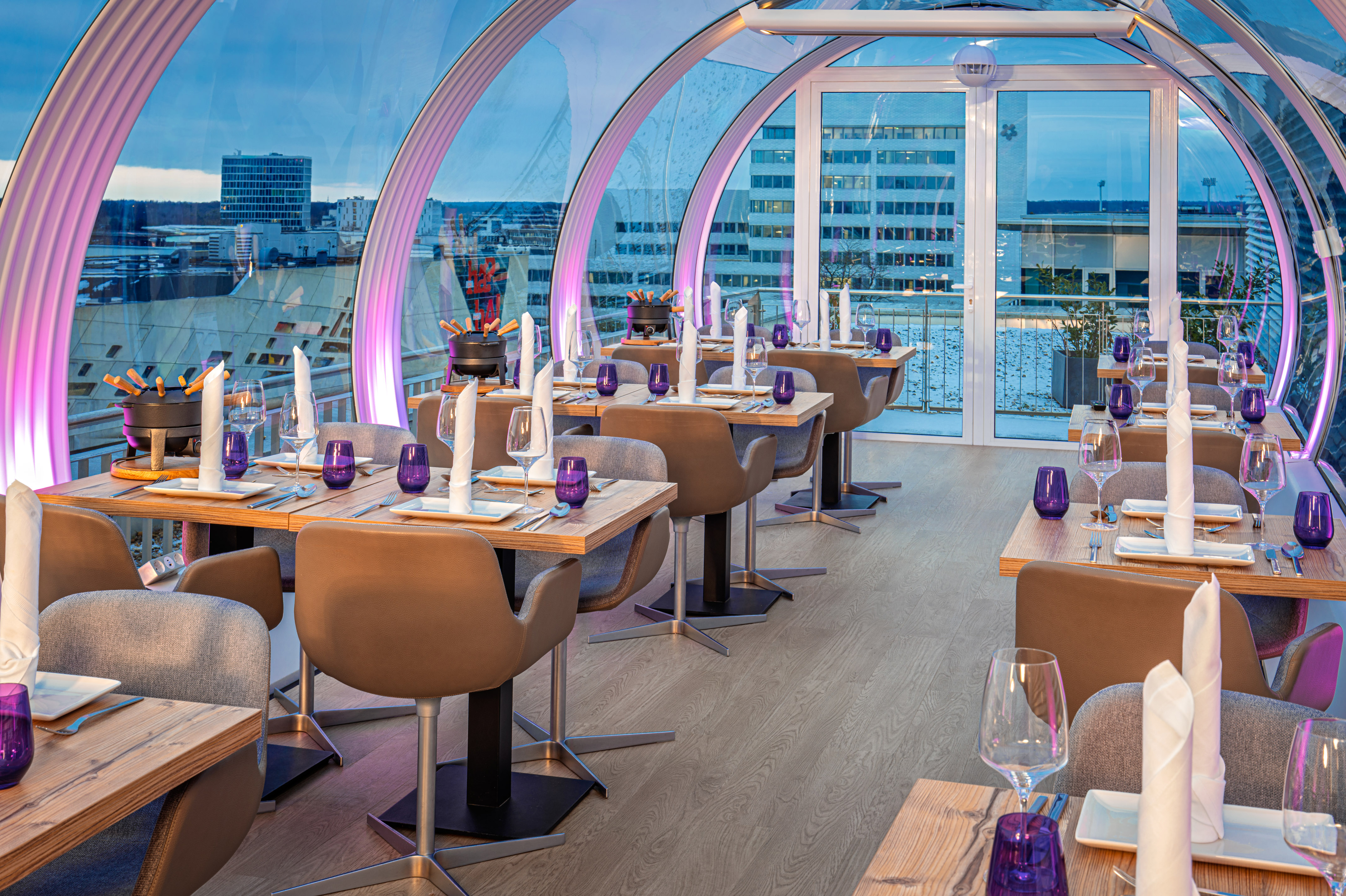 Elegant glass tunnel restaurant with city views, set tables, and fondue. - Sky Lounge & Bar The VIEW, Aperitivos - INNSiDE Wolfsburg, Wolfsburg