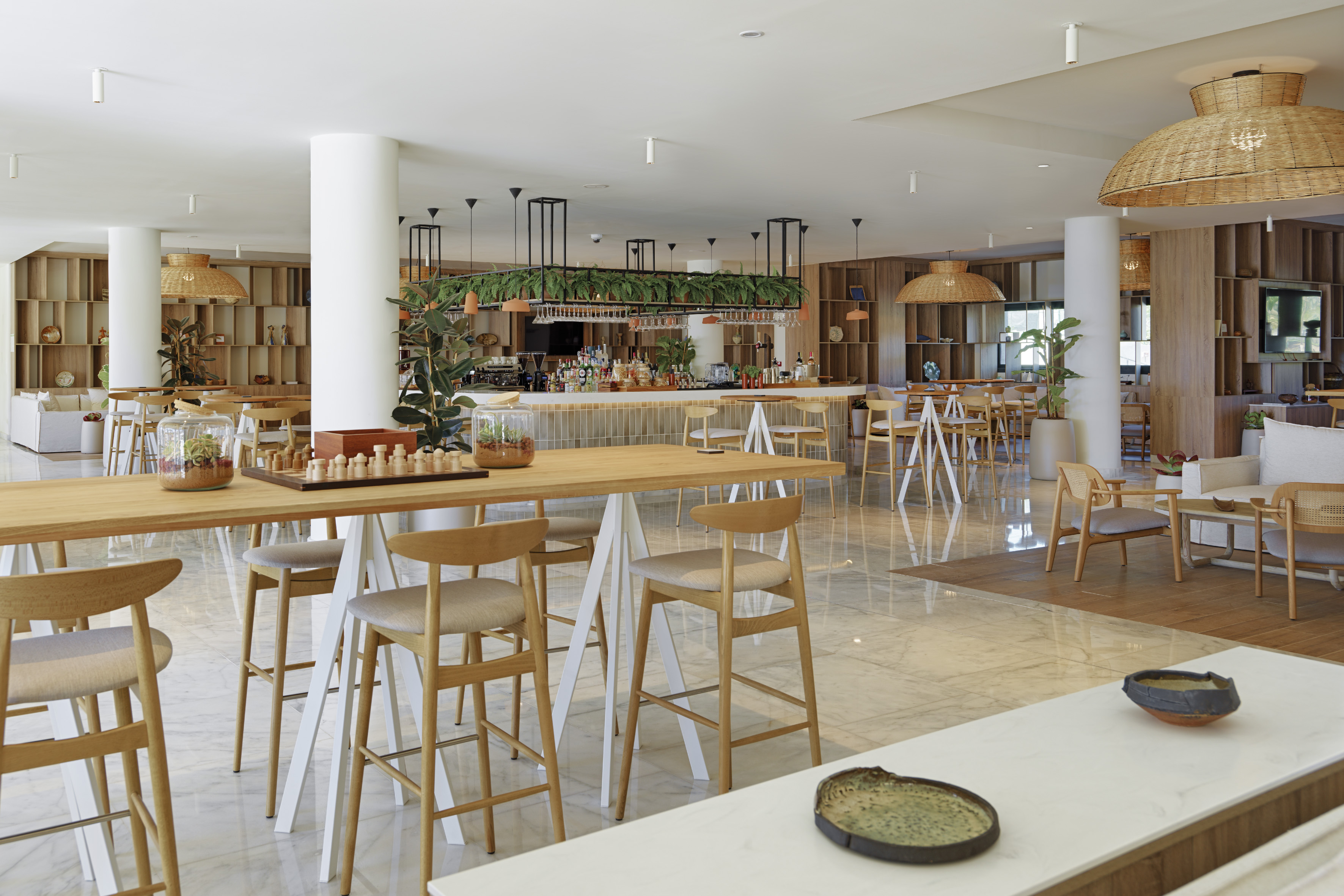 Modern hotel bar and lounge with wooden high tables, stools, and plants.