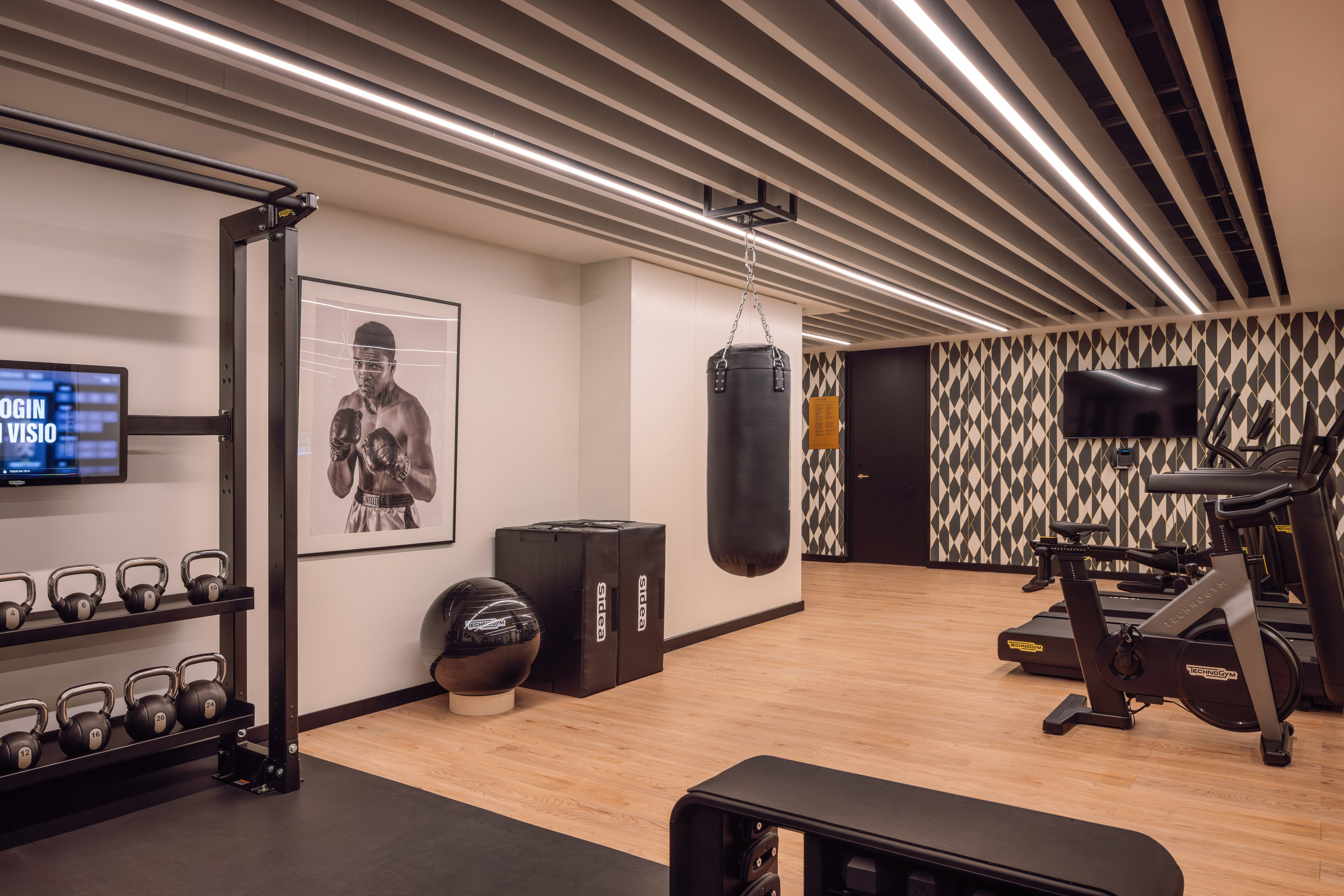 Modern fitness space with kettlebells, punching bag, Technogym bikes, and treads.