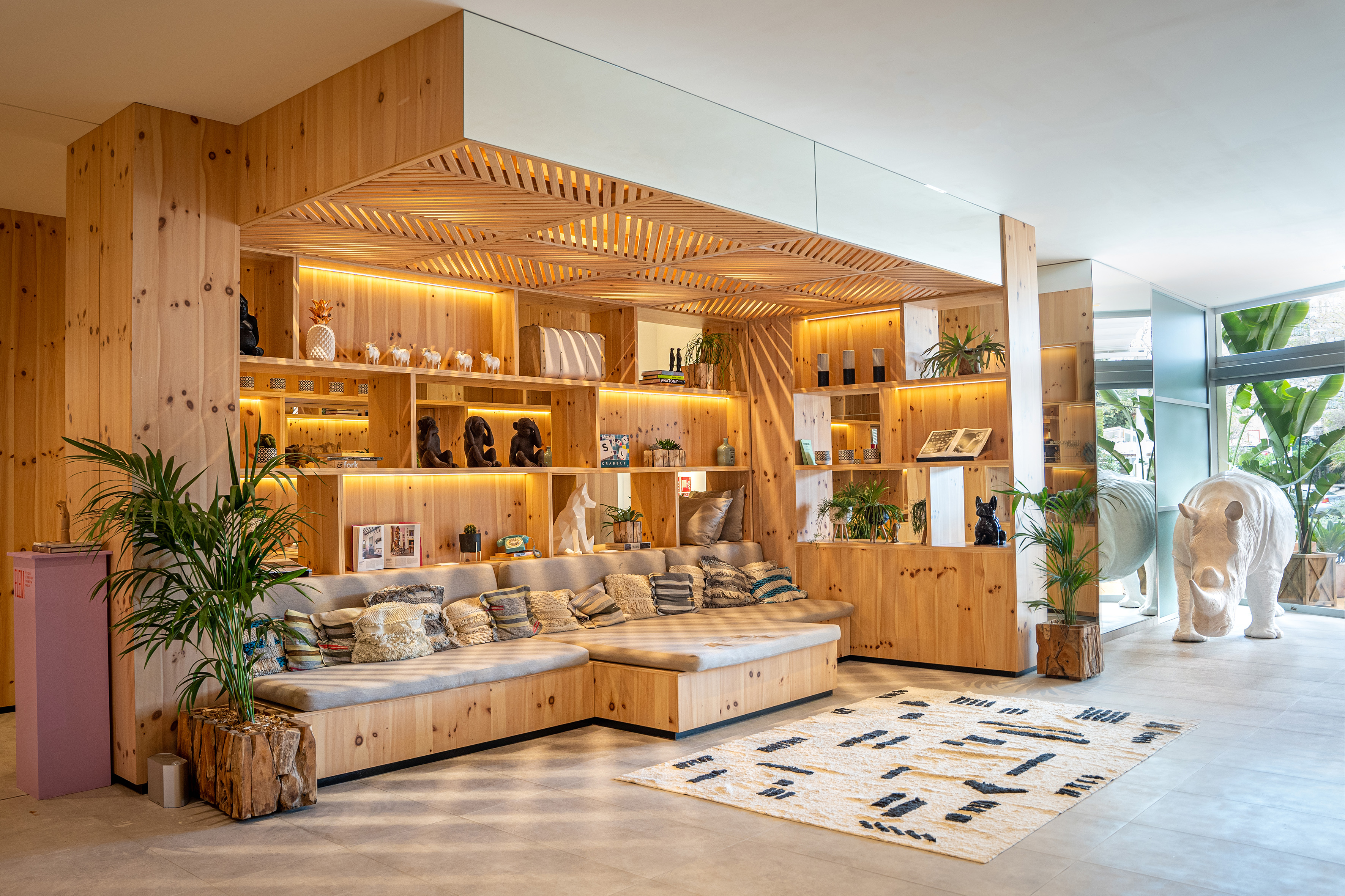 Modern wooden lounge with built-in seating, illuminated shelves, and a white rhino sculpture.