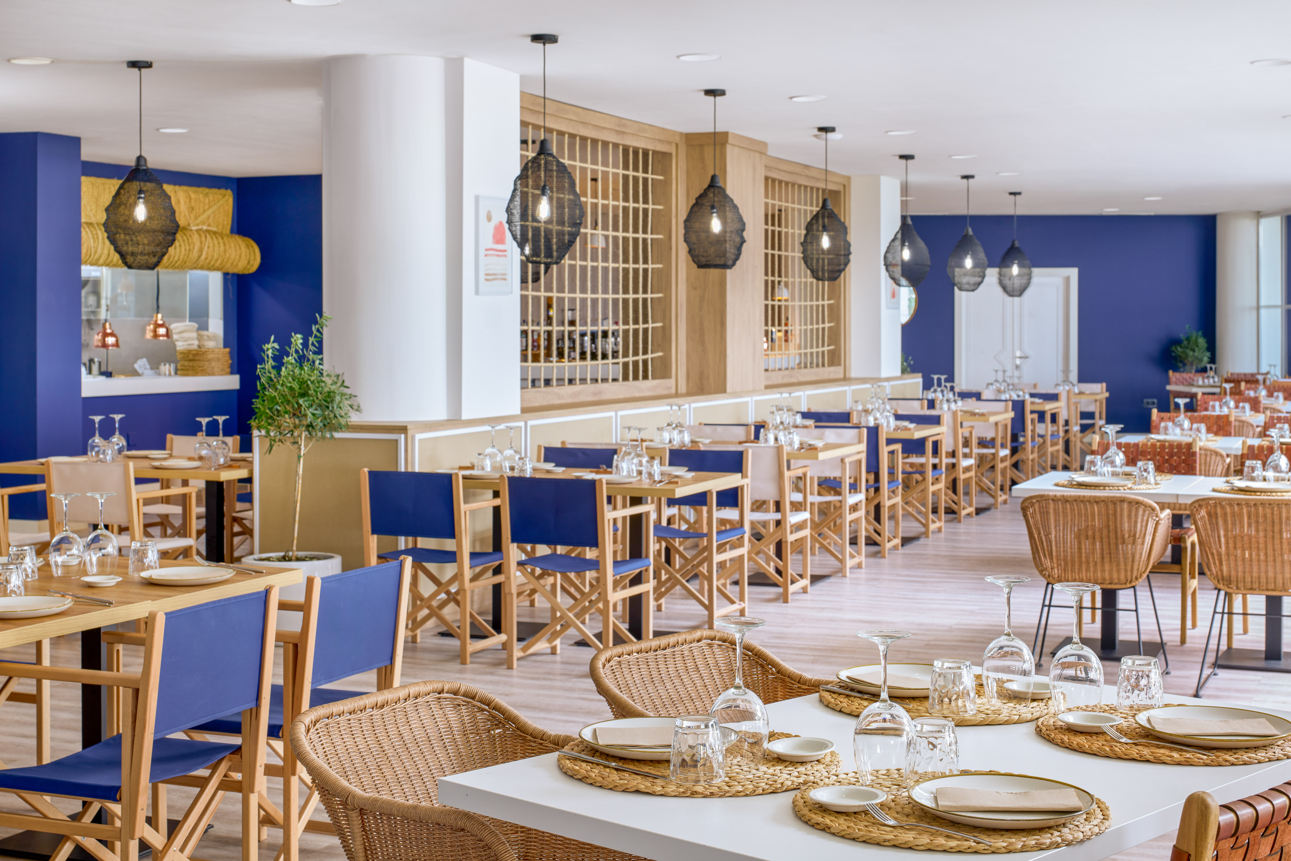 Modern blue and wood restaurant interior with wicker chairs and set tables.
