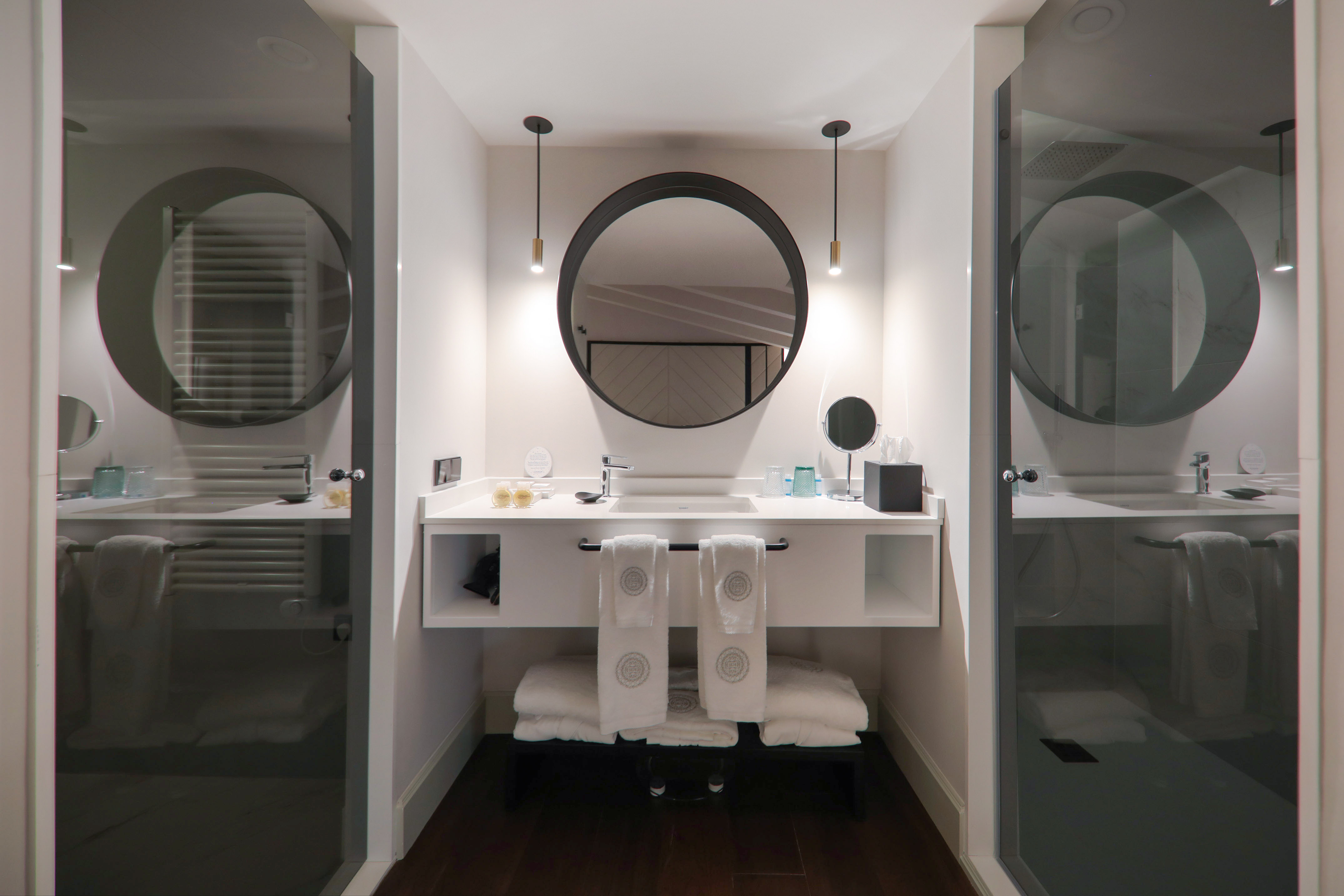 Modern hotel bathroom, vanity with round mirror, glass showers.