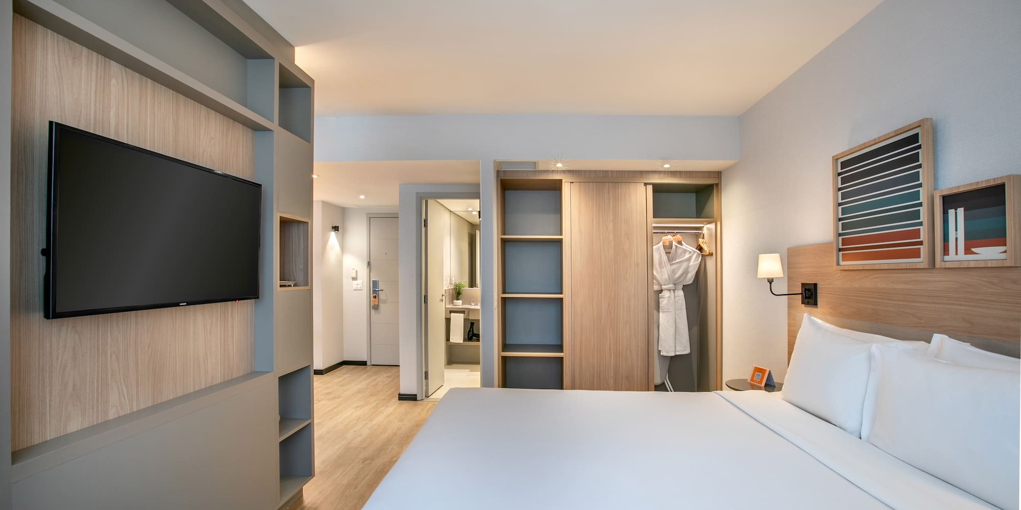Modern hotel guest room with bed, TV, built-in storage, and open closet.