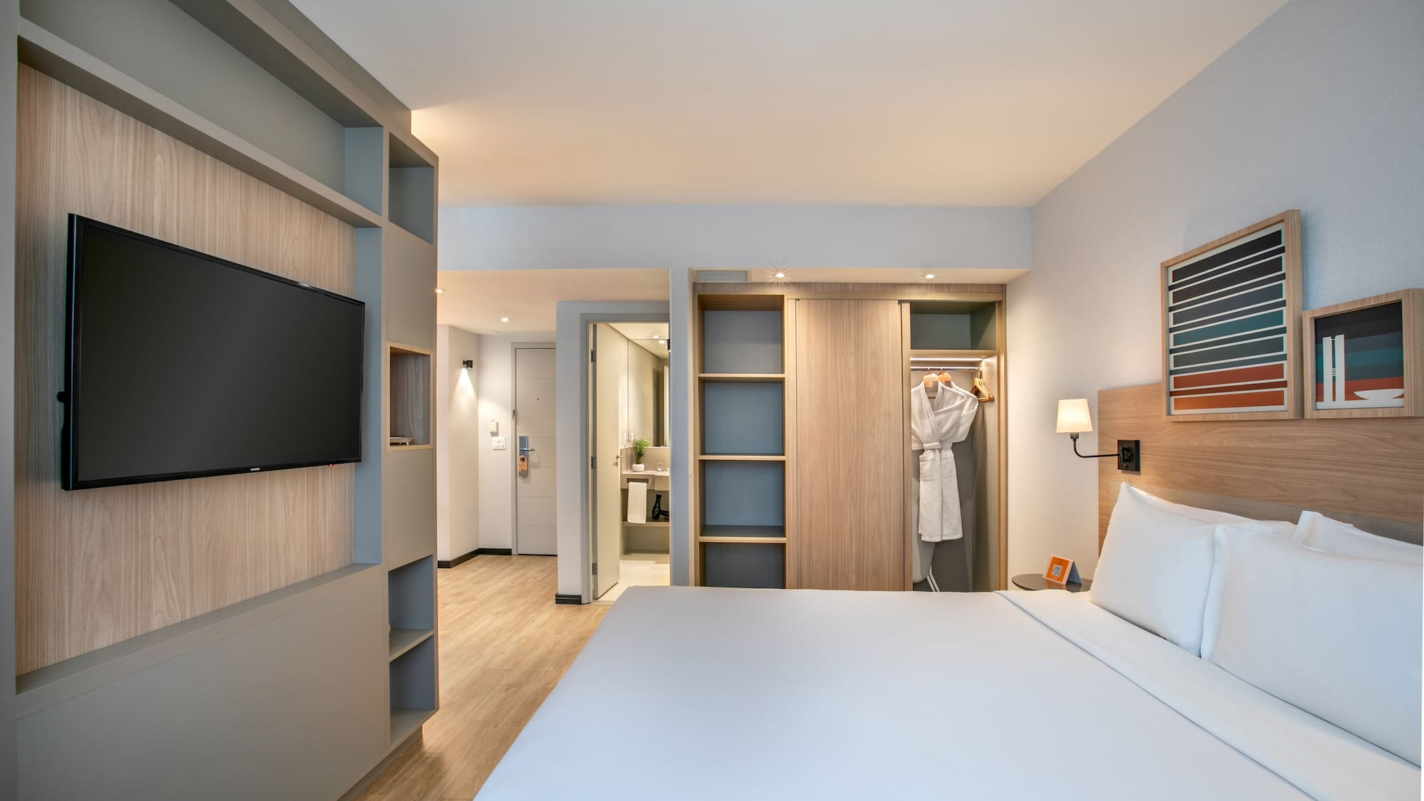 Modern hotel guest room with bed, TV, built-in storage, and open closet.