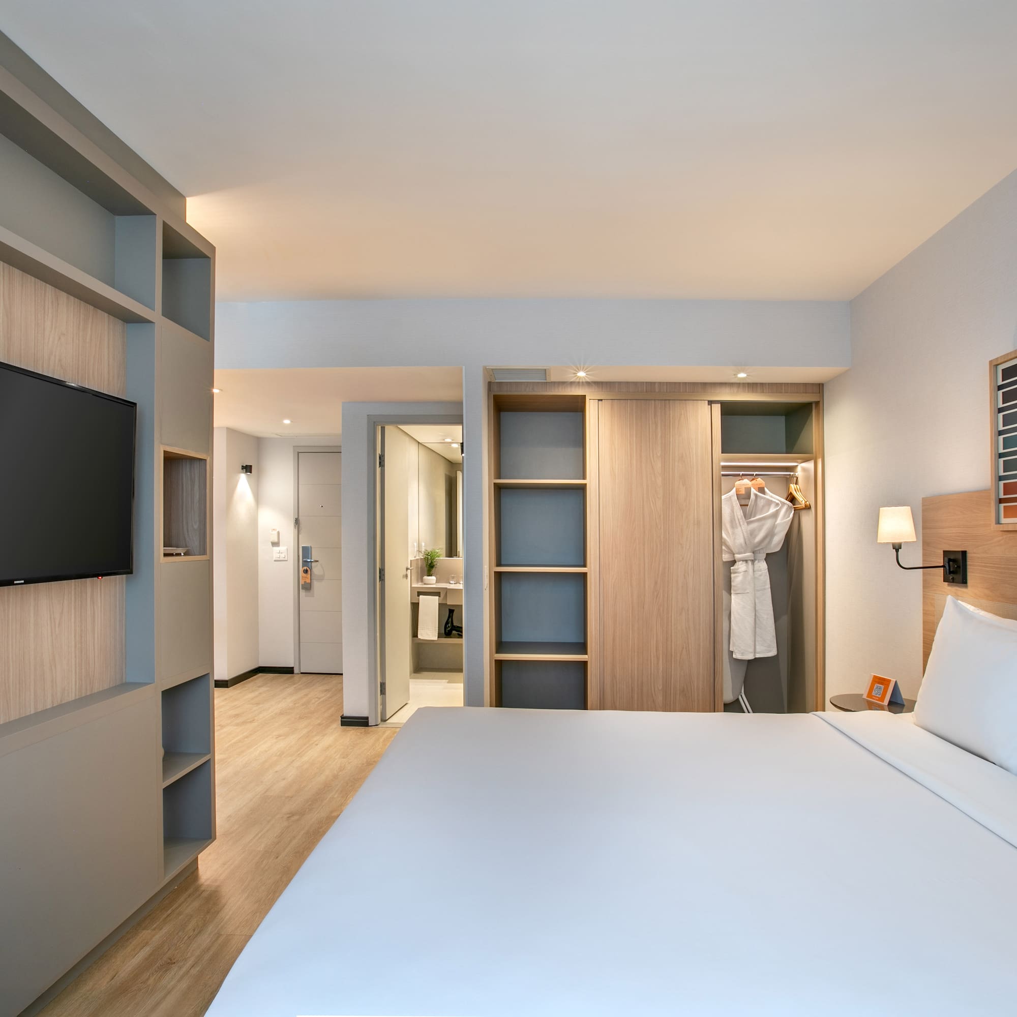 Modern hotel guest room with bed, TV, built-in storage, and open closet.