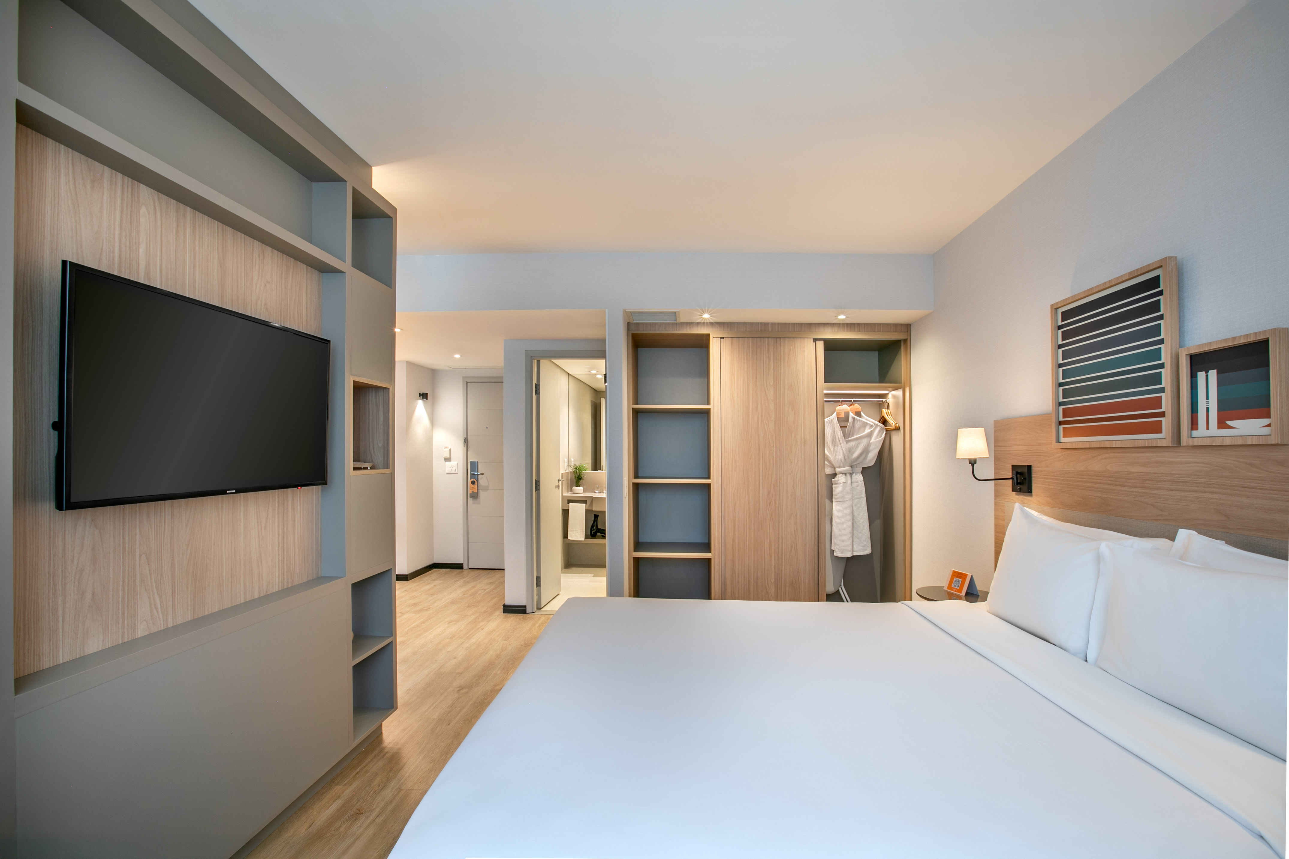 Modern hotel guest room with bed, TV, built-in storage, and open closet.