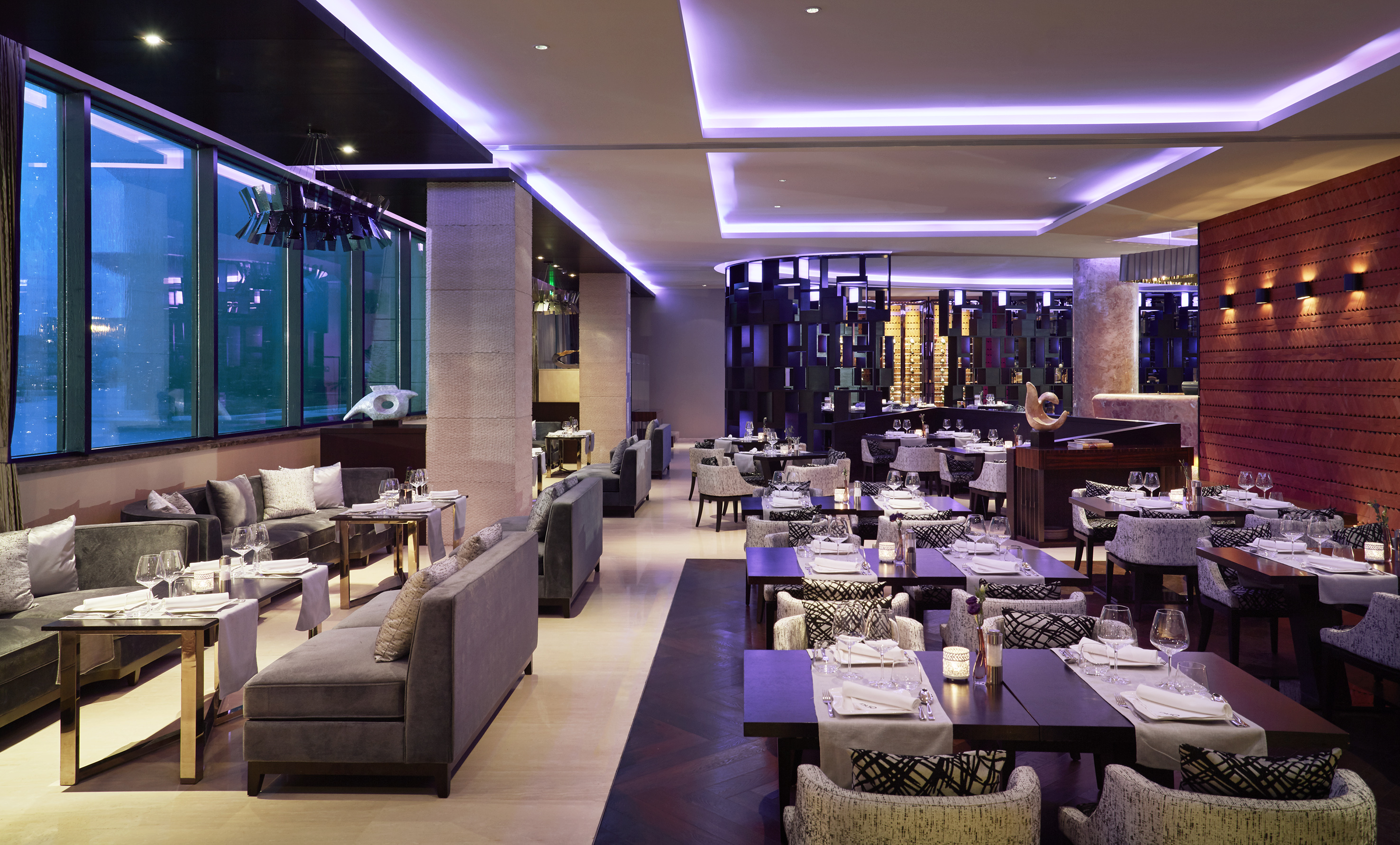 Modern restaurant with purple lighting, elegant tables, and lounge seating.