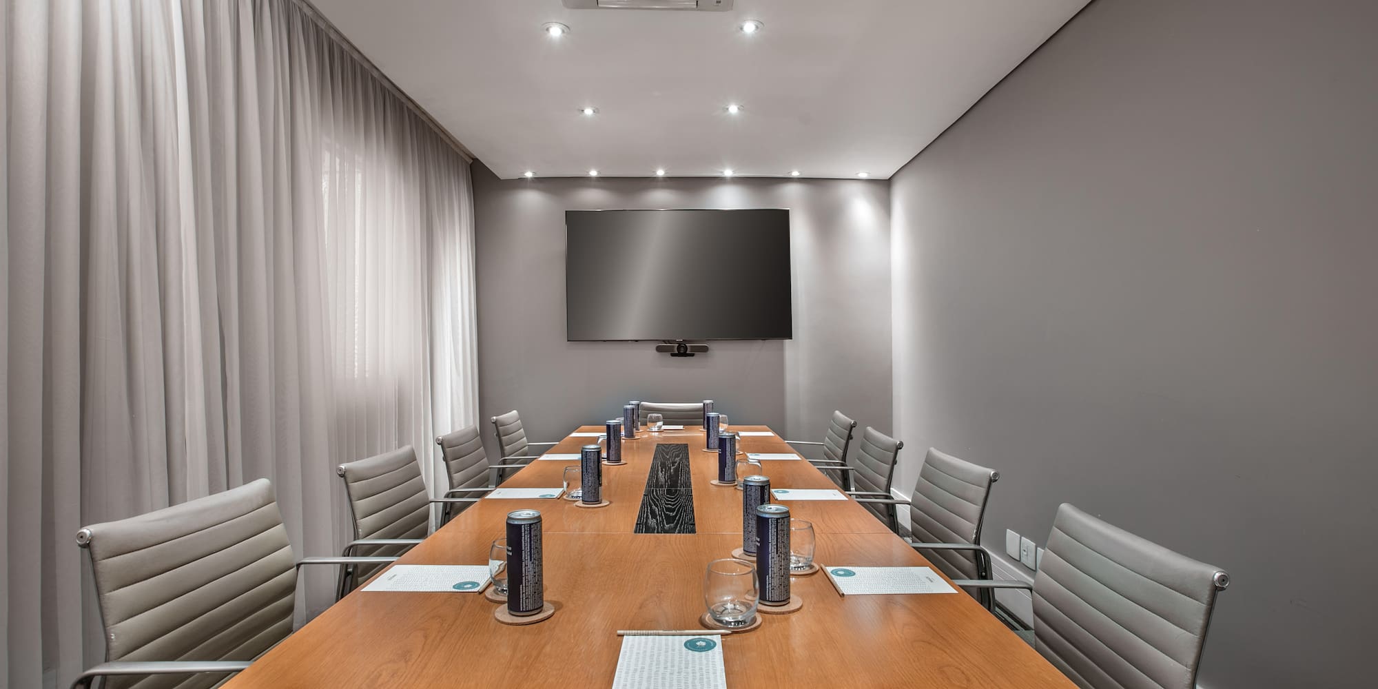 Stylish meeting room with long wooden table, grey chairs, and wall TV.
