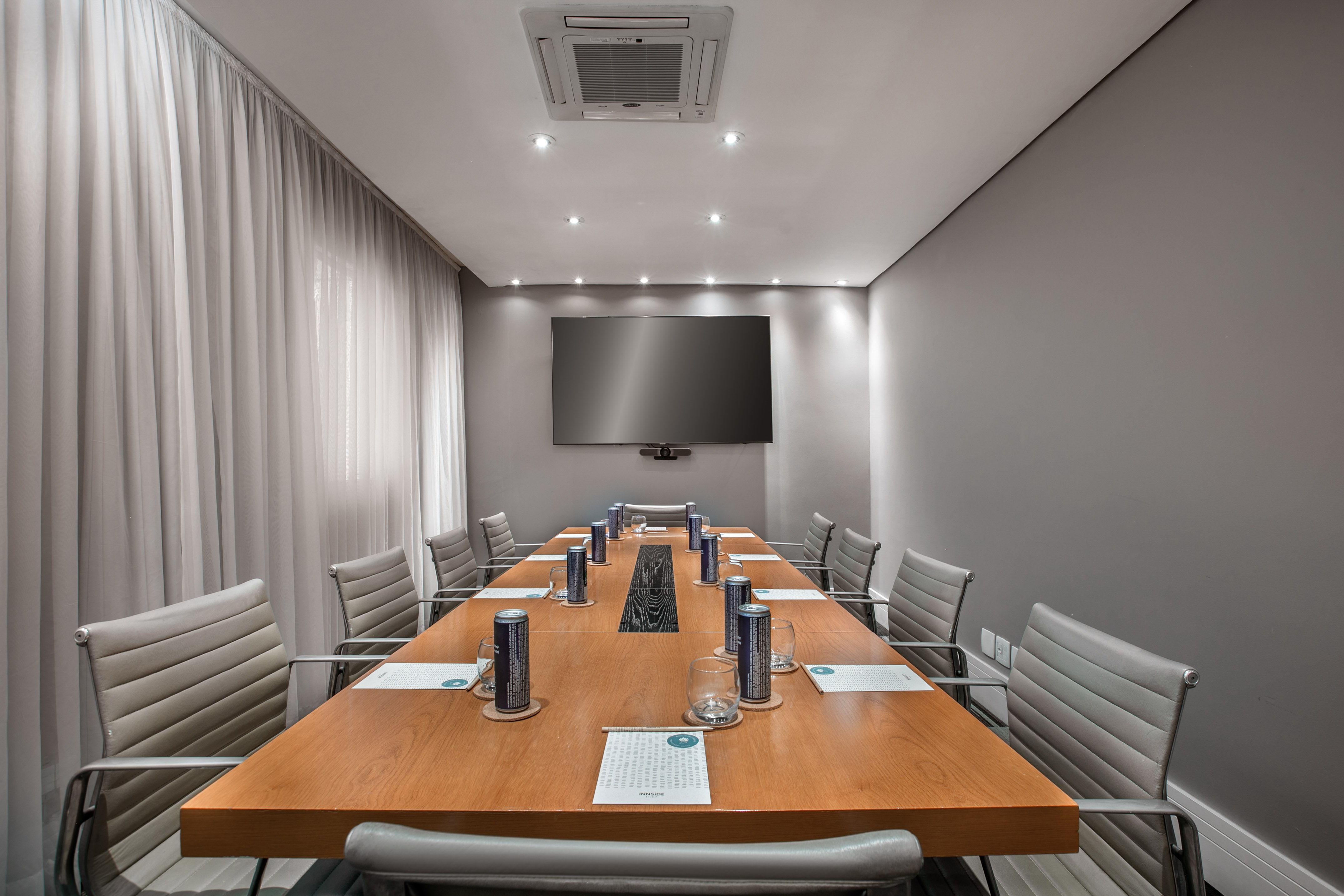 Stylish meeting room with long wooden table, grey chairs, and wall TV.