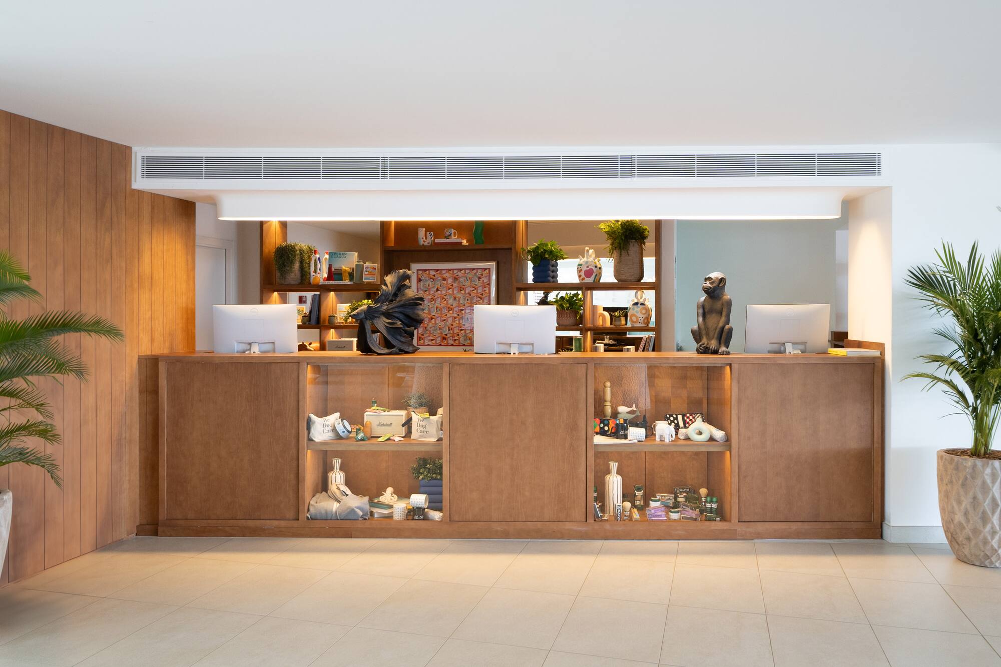 Modern wooden reception desk with computers, decorative objects, and shelving.
