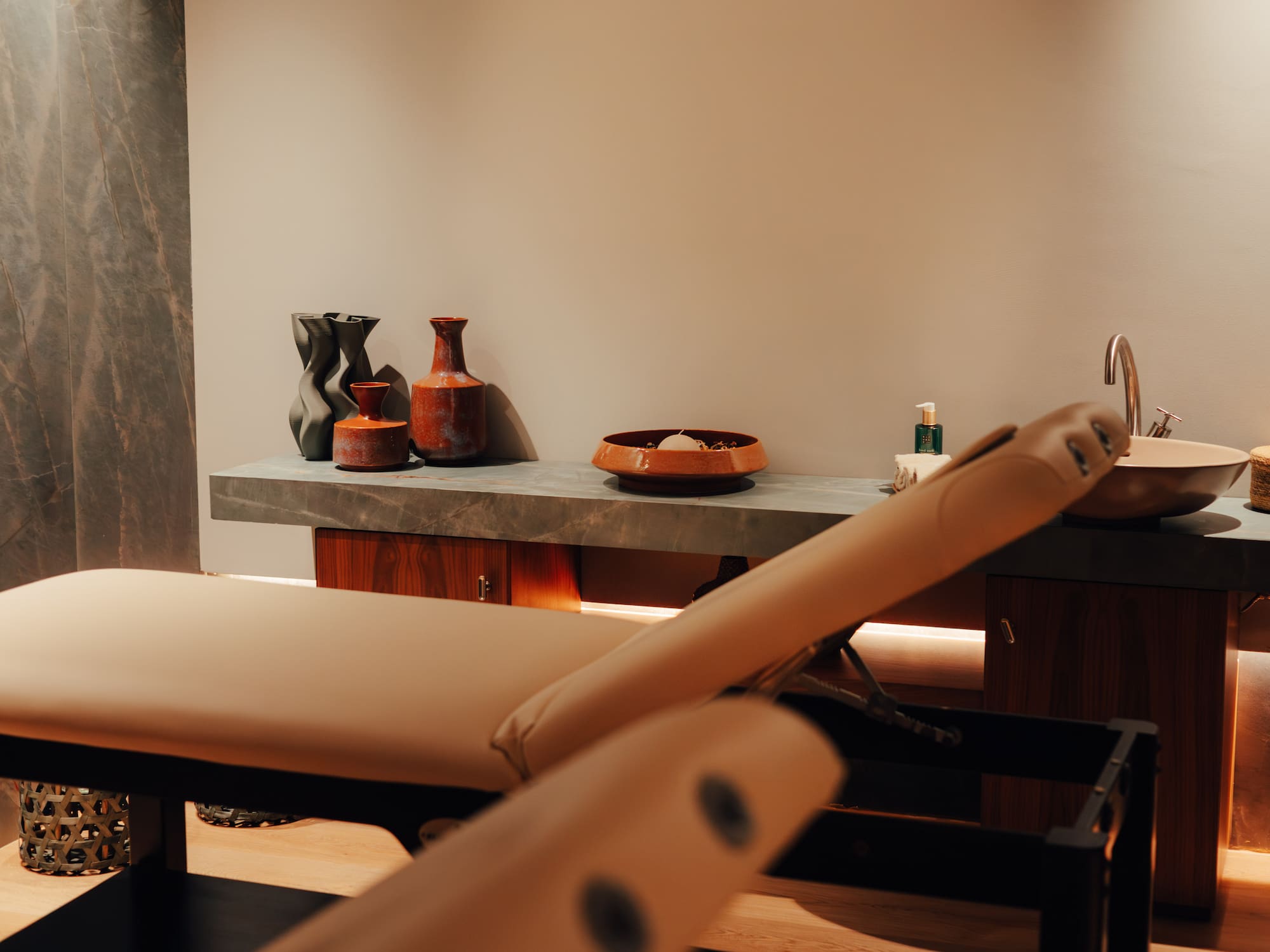 Warm spa treatment room with two beige massage beds and pampas grass decor.