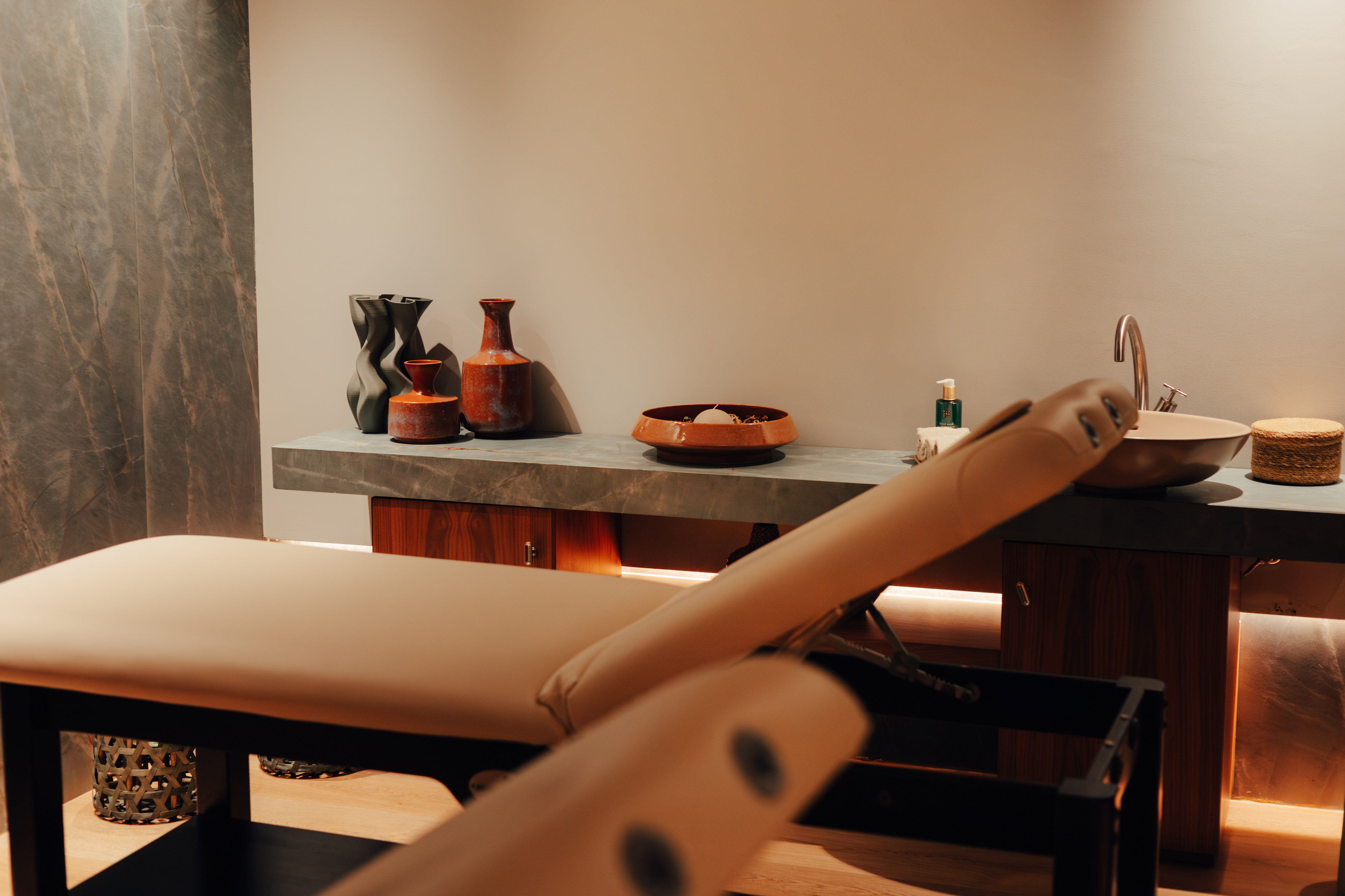 Warm spa treatment room with two beige massage beds and pampas grass decor.