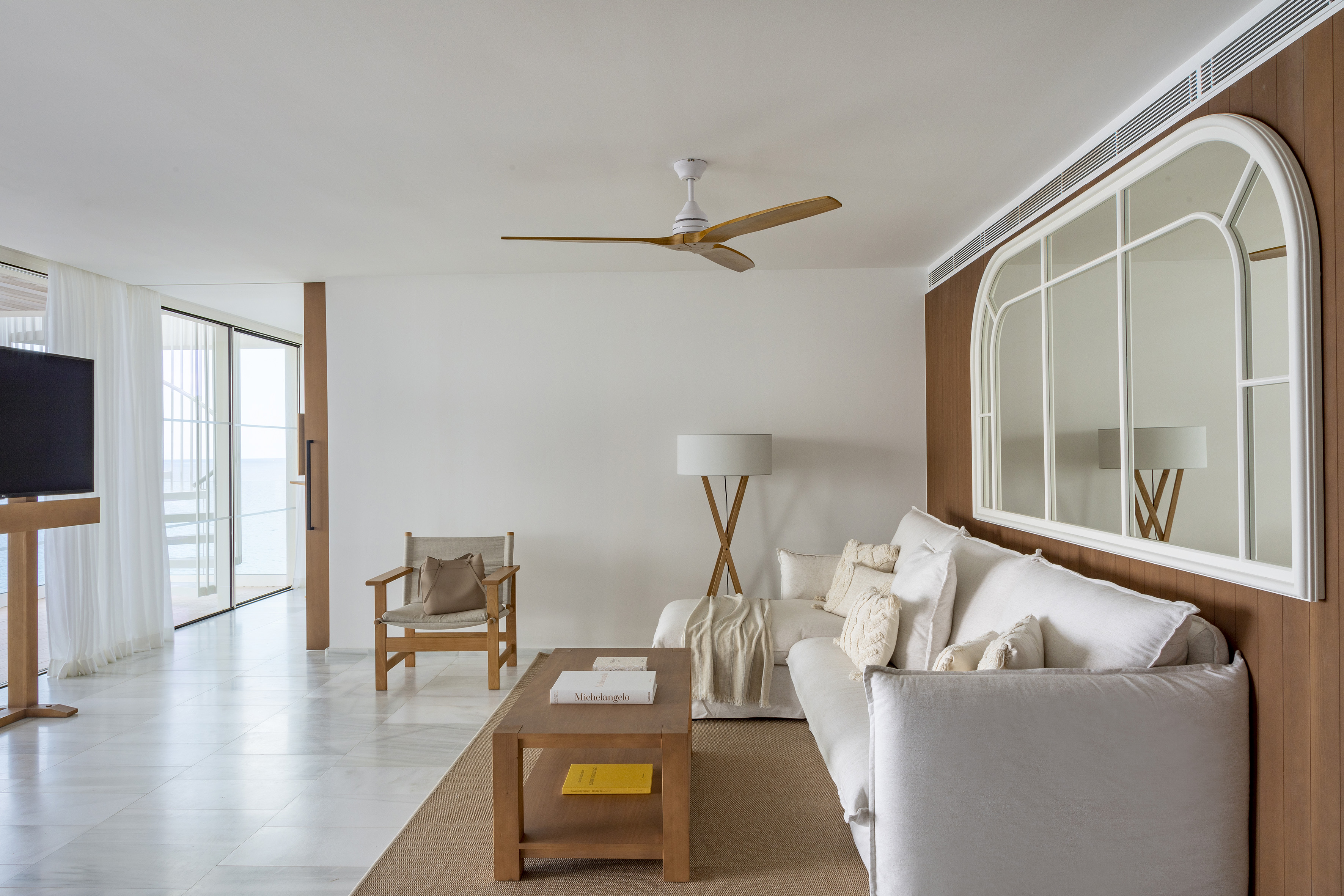 Bright coastal living room with white sofa, wood accents, and ceiling fan.