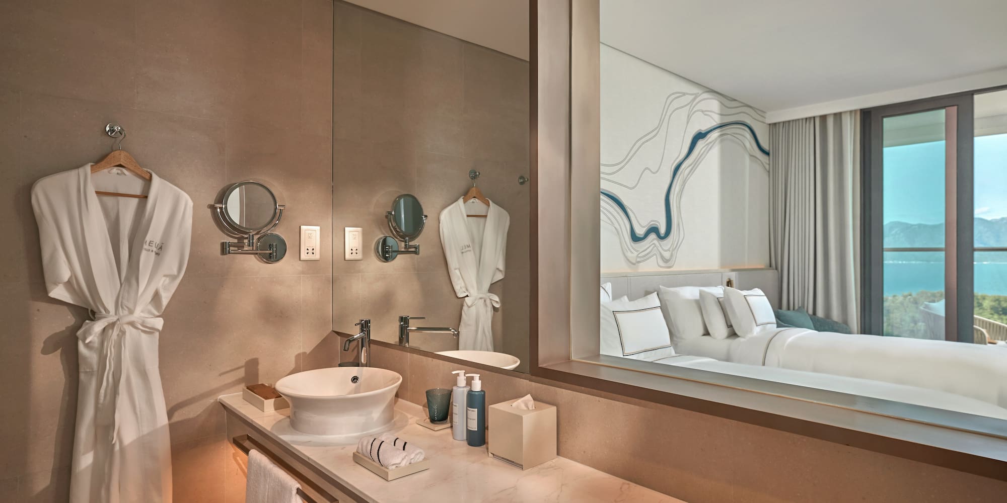 Modern hotel bathroom vanity, marble counter, mirror reflects bedroom, sea view.