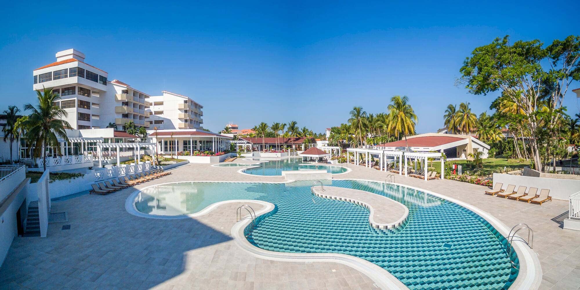 a pool with a curved design and a white structure with palm trees