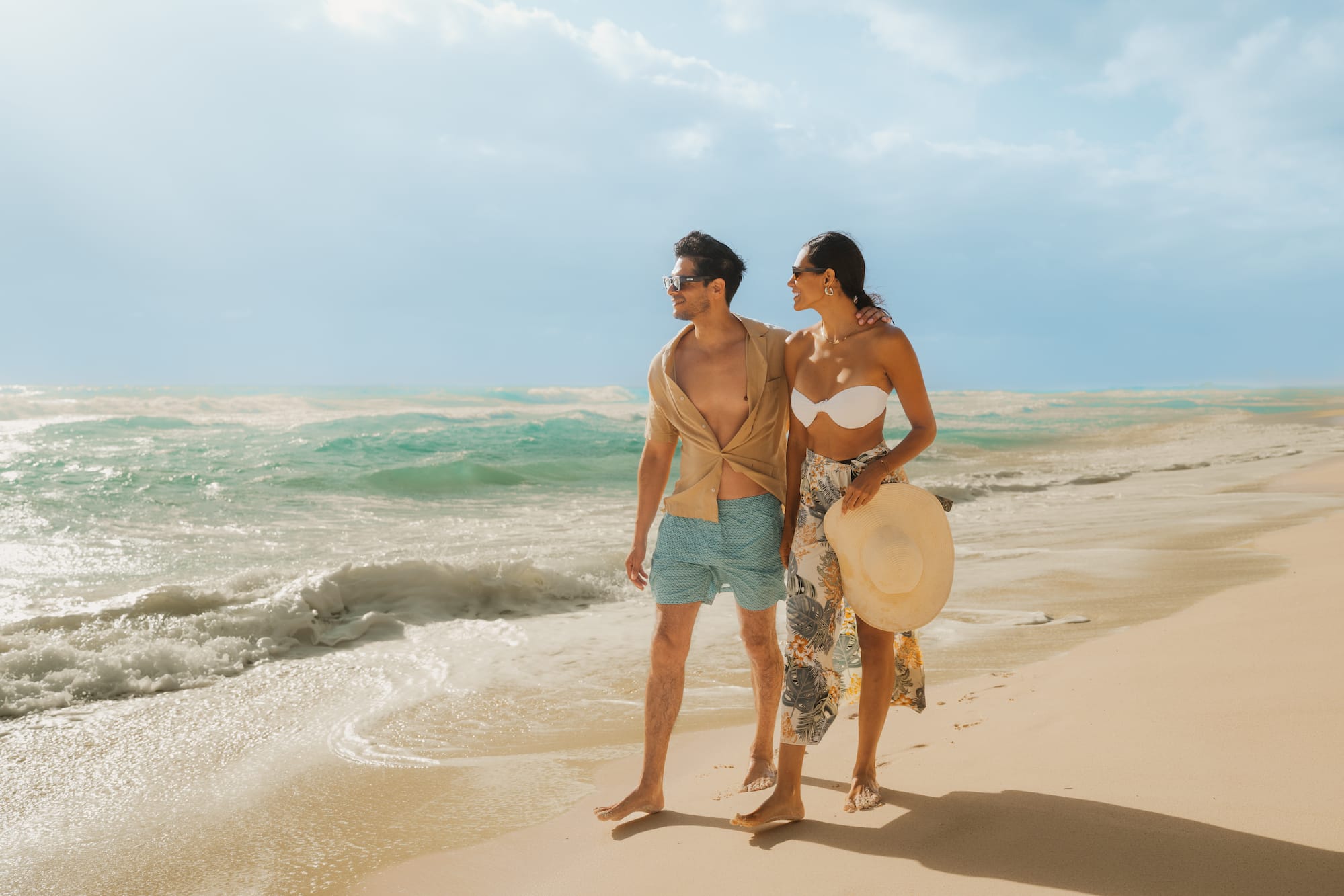 Pareja joven camina descalza en playa tropical junto al mar azul.