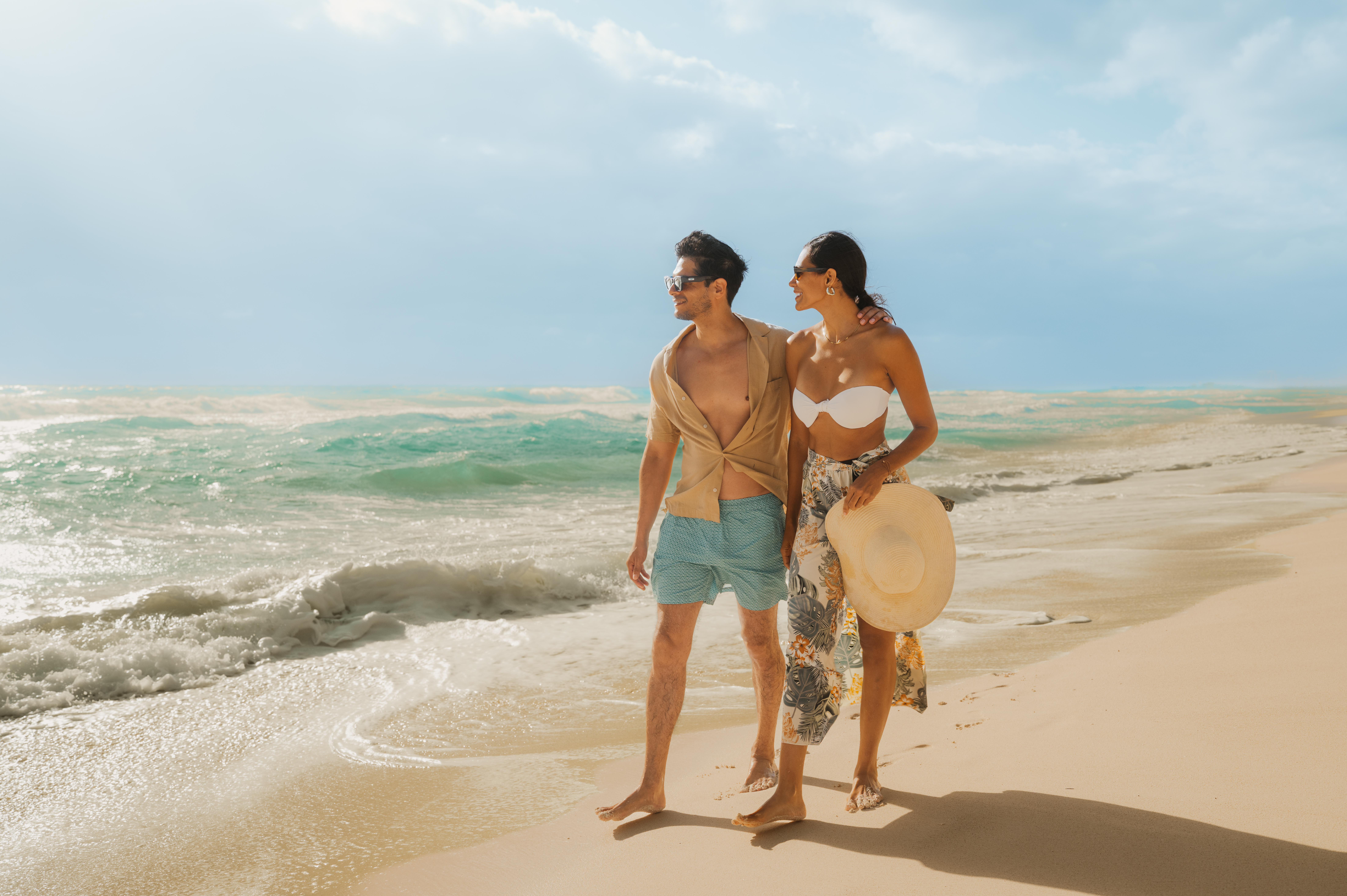 Pareja joven camina descalza en playa tropical junto al mar azul.