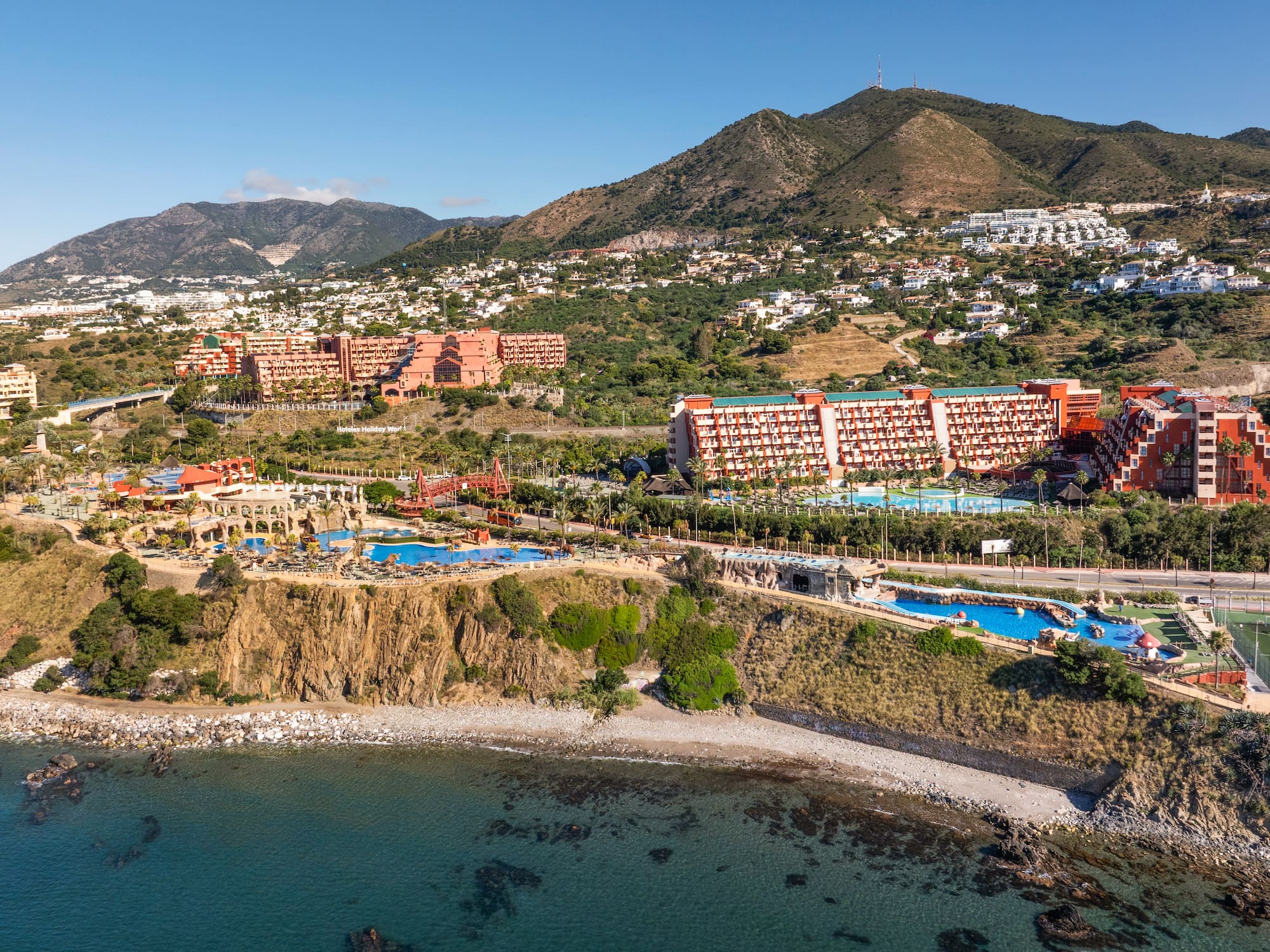 Benalmádena Holiday World resort: hotels, pools, rocky beach, mountains.