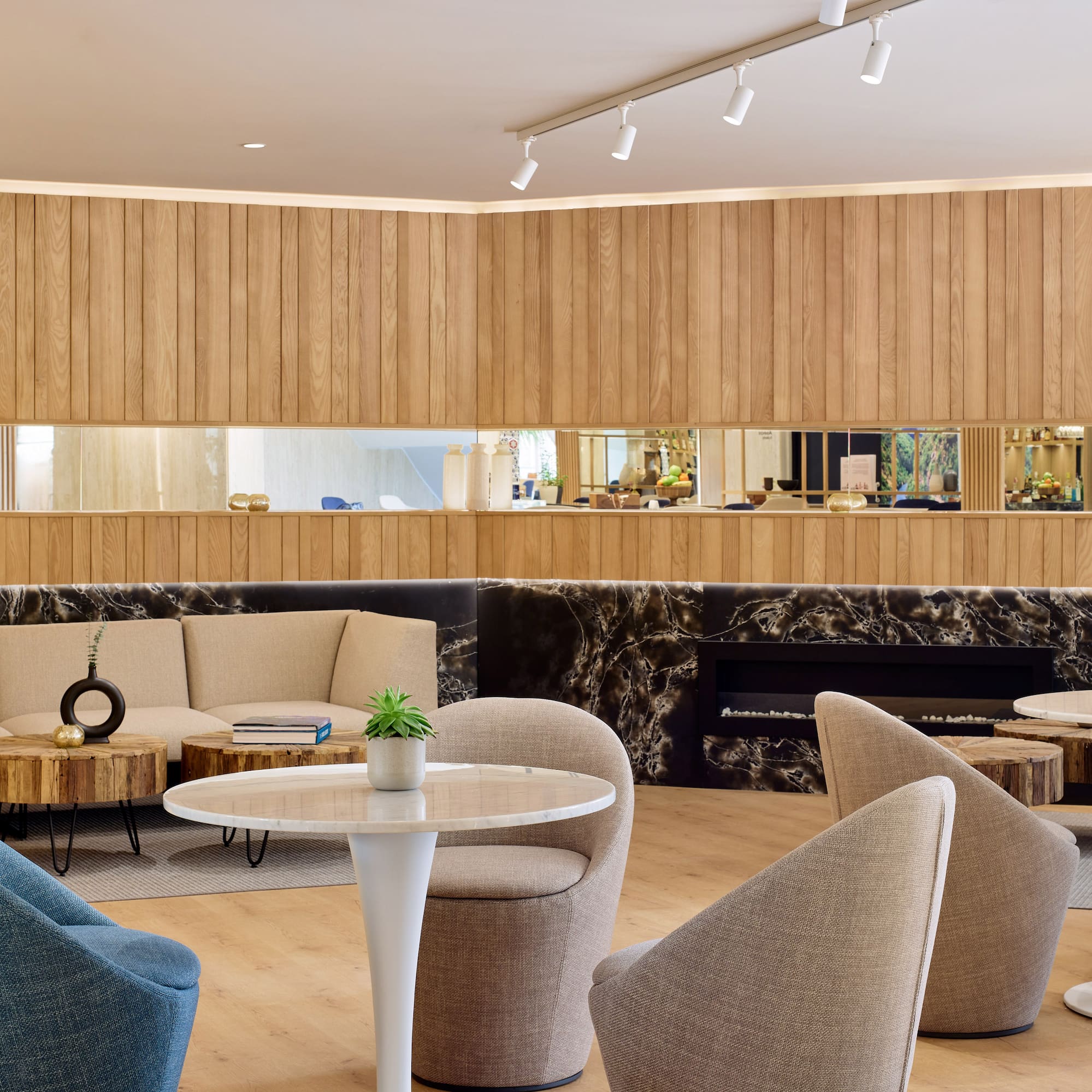 Lounge moderno hotel con paneles madera, sofás beige y mesa mármol.