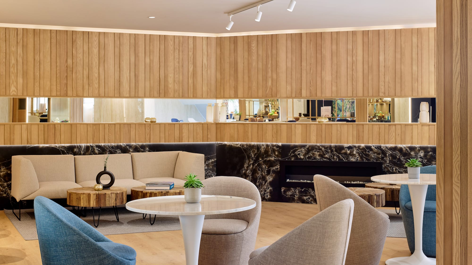 Lounge moderno con paneles de madera, sofá beige, sillones y detalles de mármol.