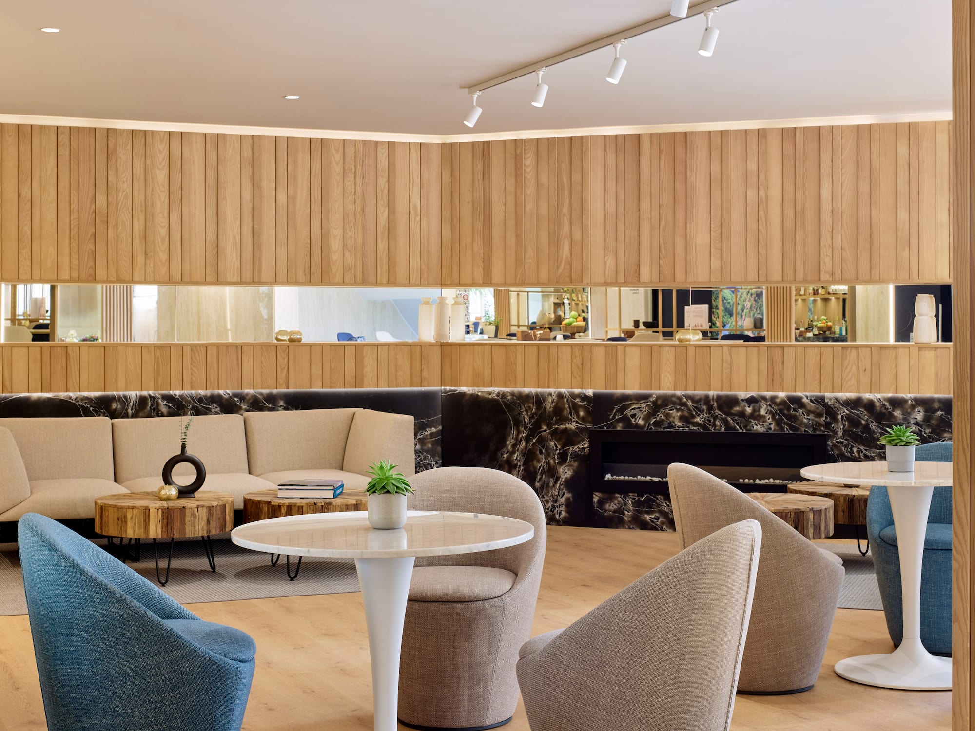 Lounge moderno hotel con paneles madera, sofás beige y mesa mármol.