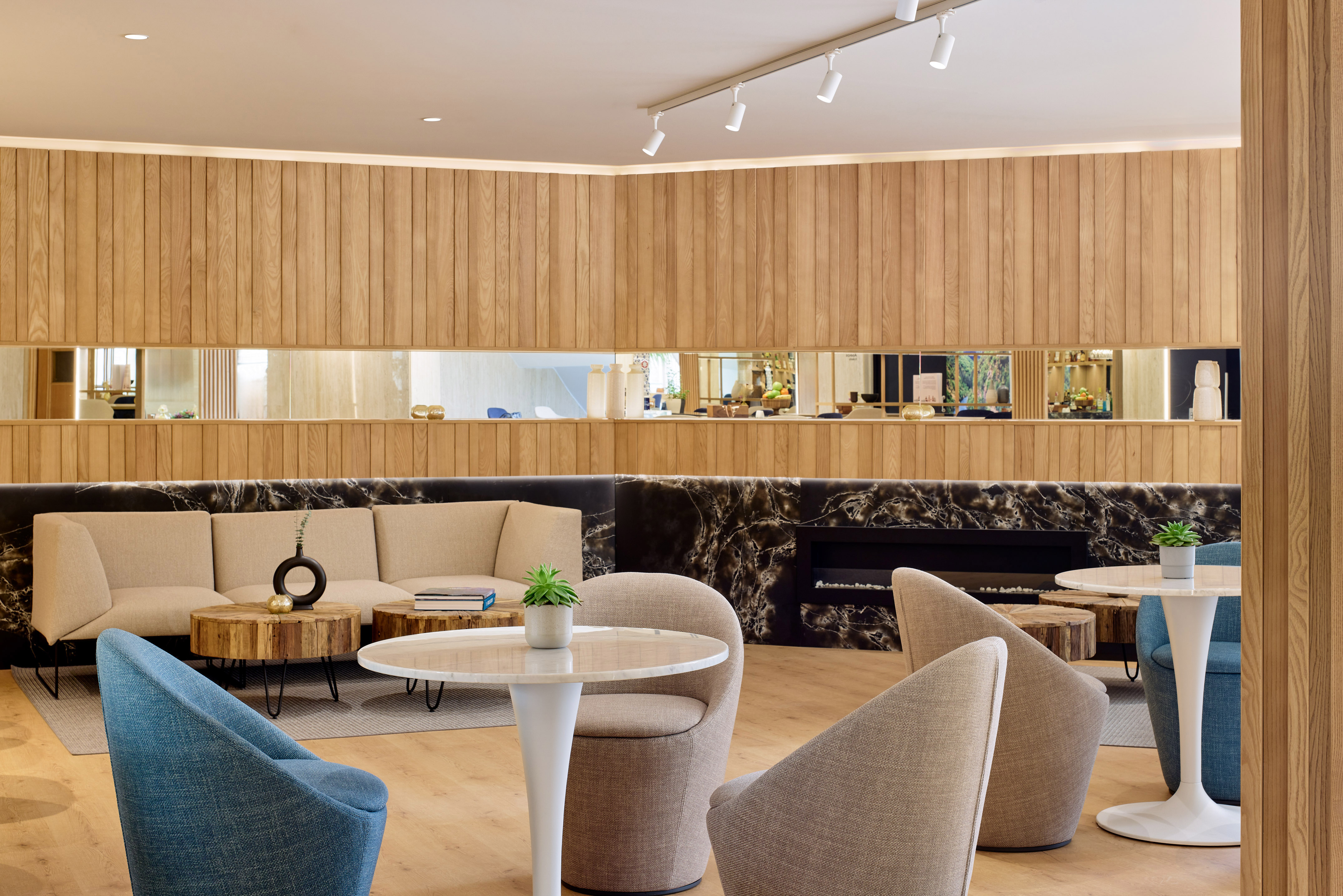 Lounge moderno hotel con paneles madera, sofás beige y mesa mármol.