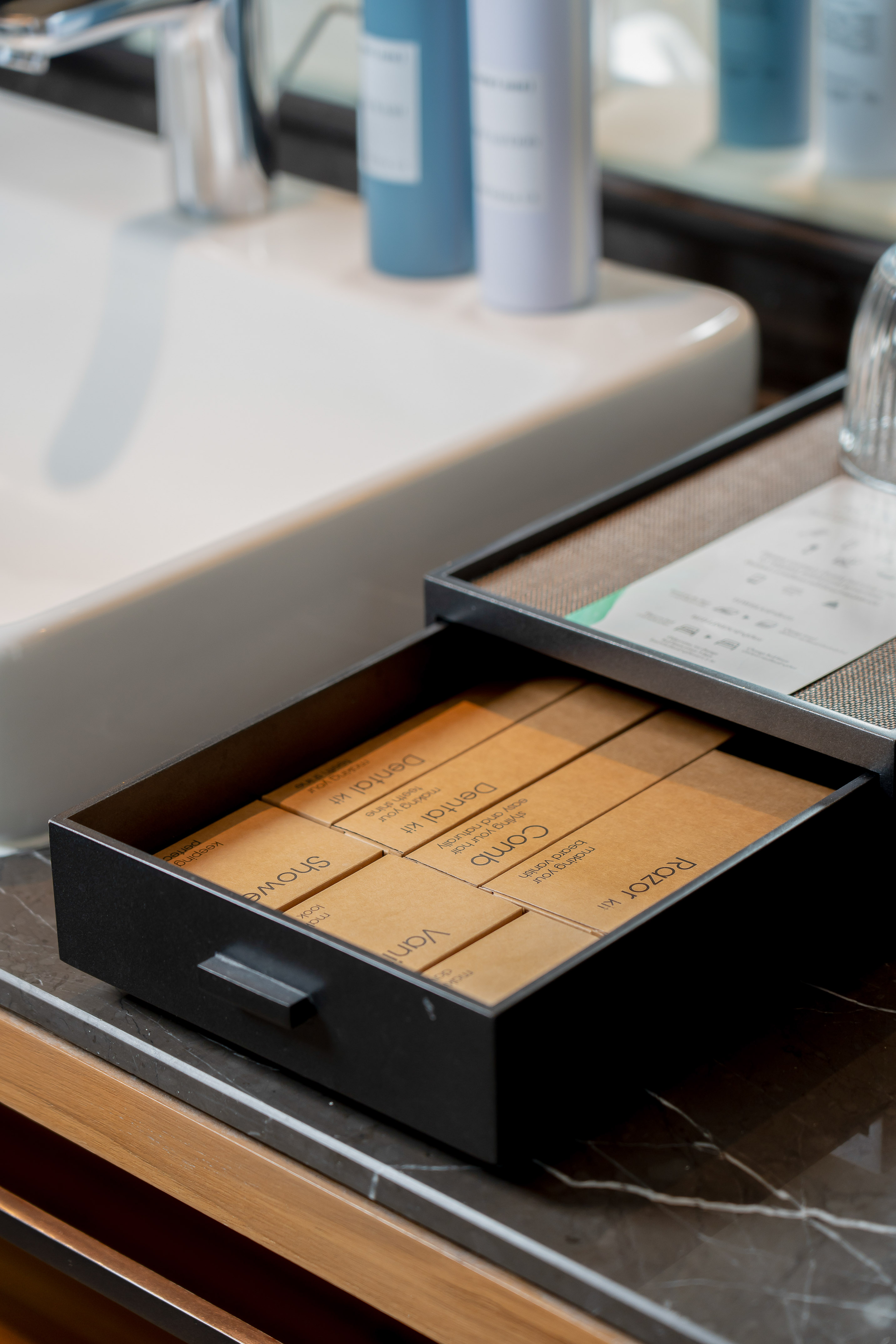 Hotel bathroom amenities: dental kit, comb, razor in an open drawer.