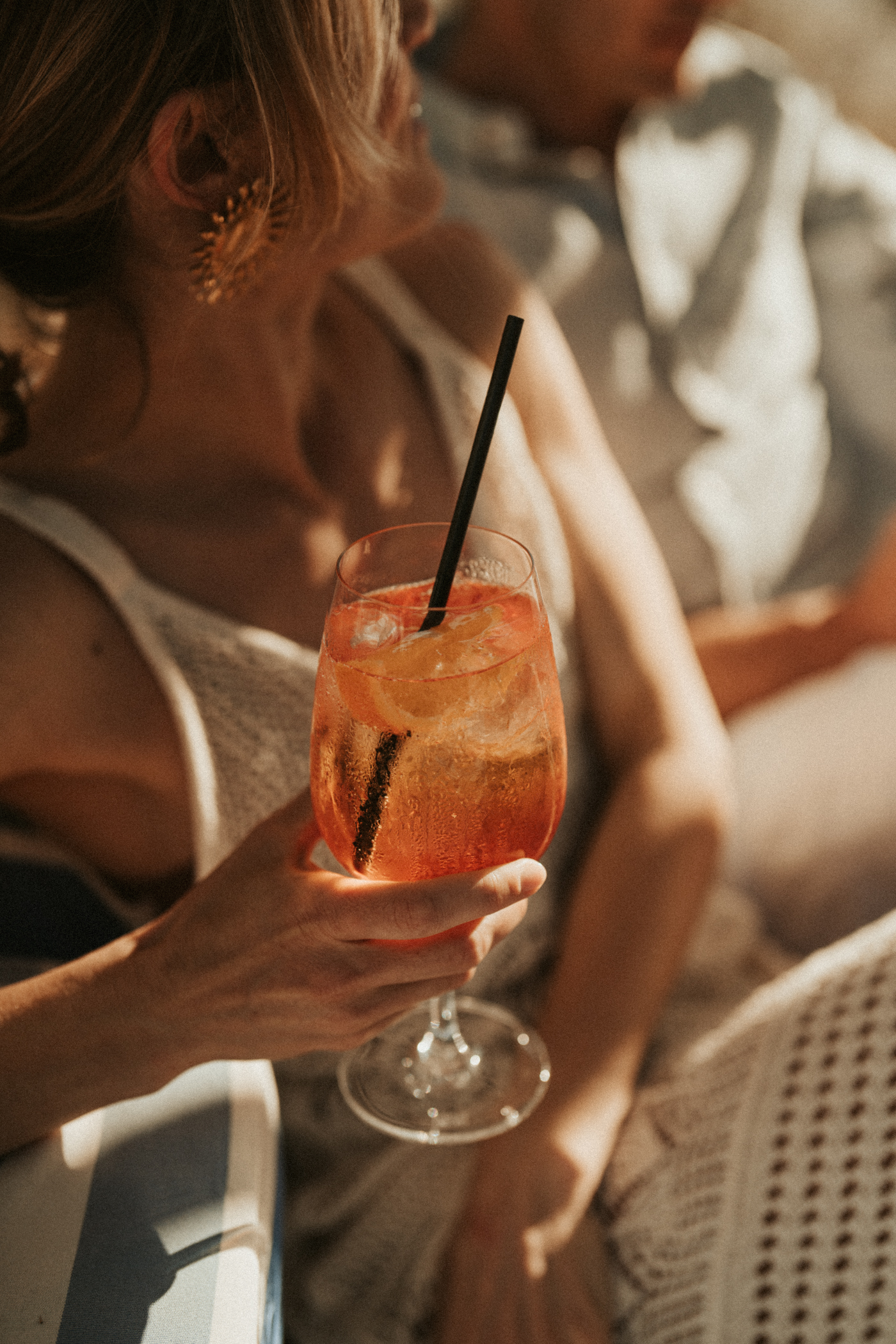 Hand holding a vibrant Aperol Spritz cocktail with ice and orange in warm light.