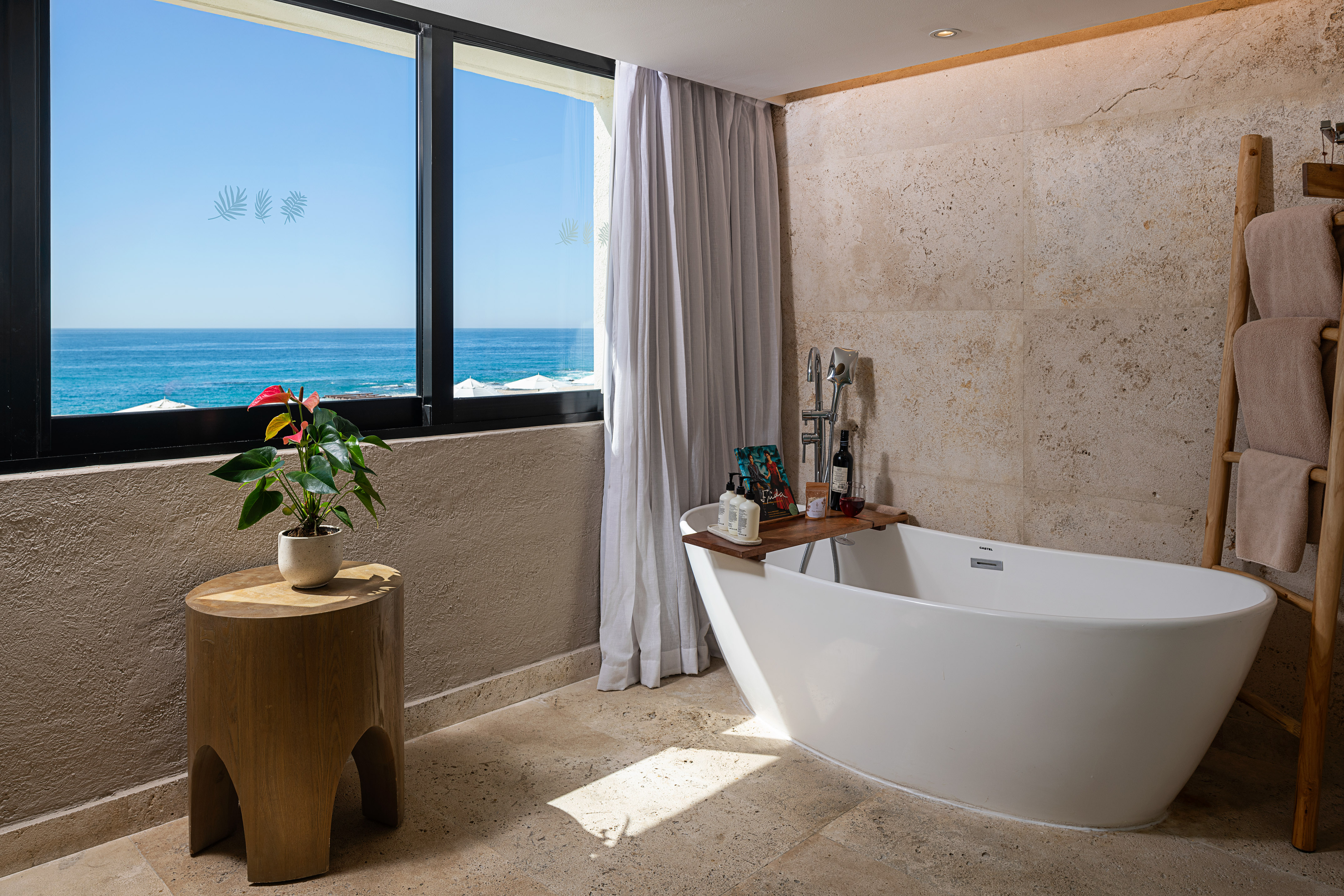 Luxury ocean view bathroom with freestanding tub and stone walls.
