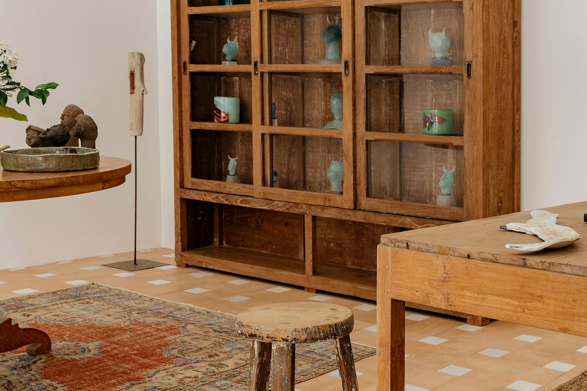 Carved wooden display cabinet with glass, terracotta floor, and woven rugs.