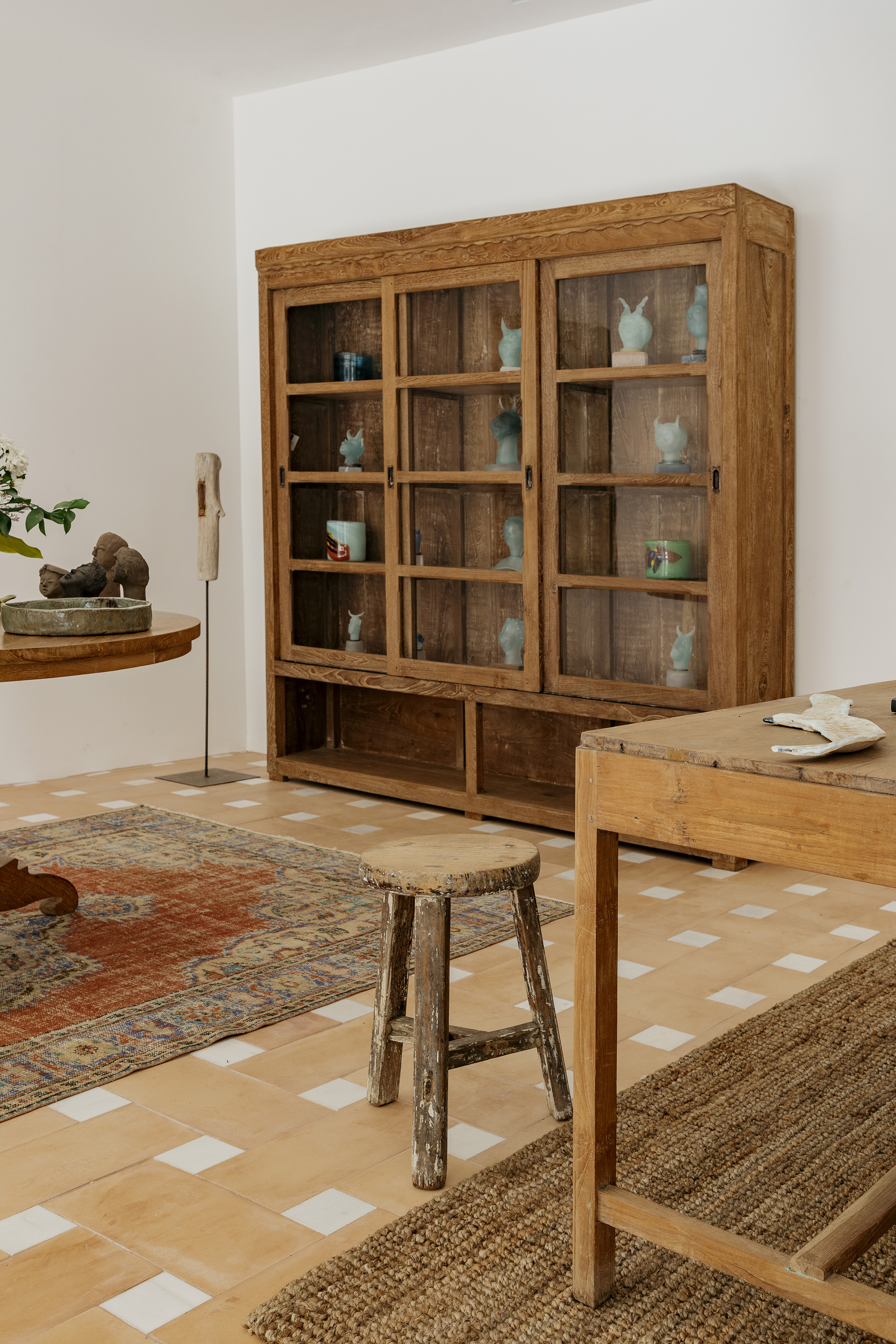 Carved wooden display cabinet with glass, terracotta floor, and woven rugs.