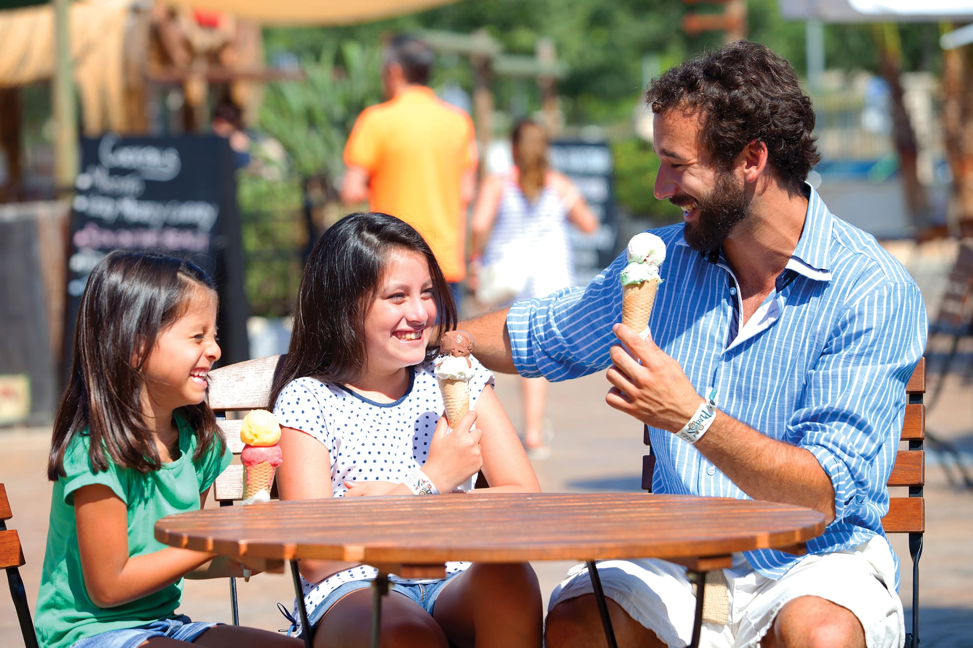 Padre e hijas felices comiendo helado al aire libre.
