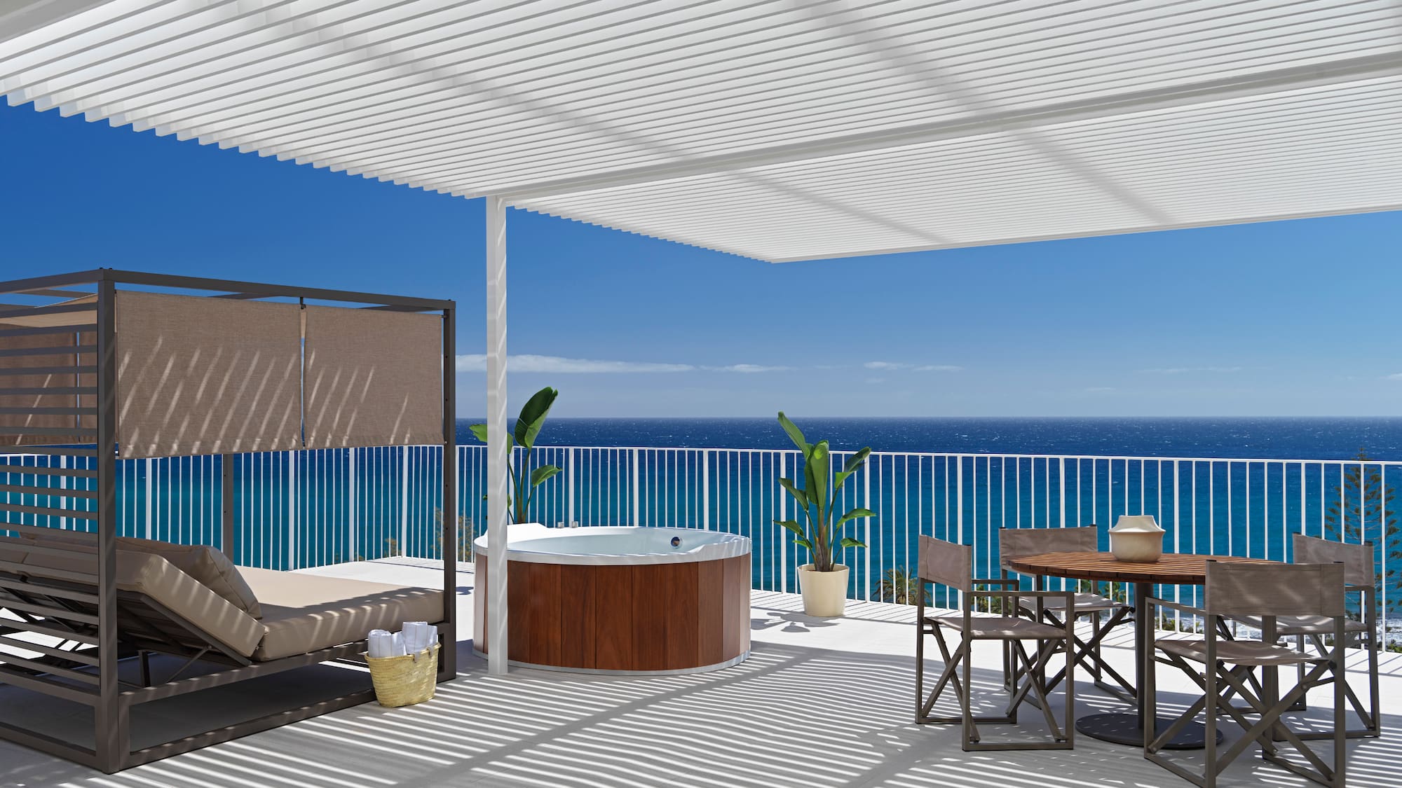 a deck with a hot tub and a table and chairs overlooking the ocean