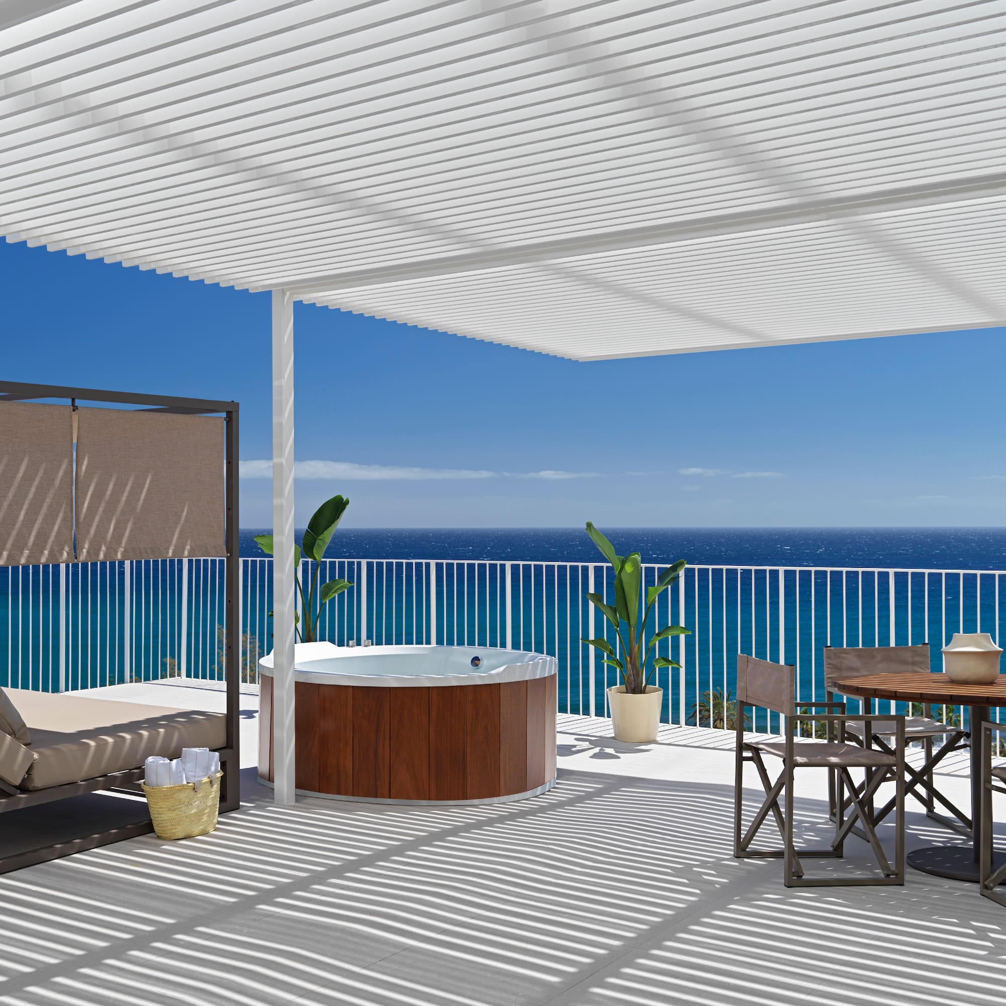 a deck with a hot tub and a table and chairs overlooking the ocean