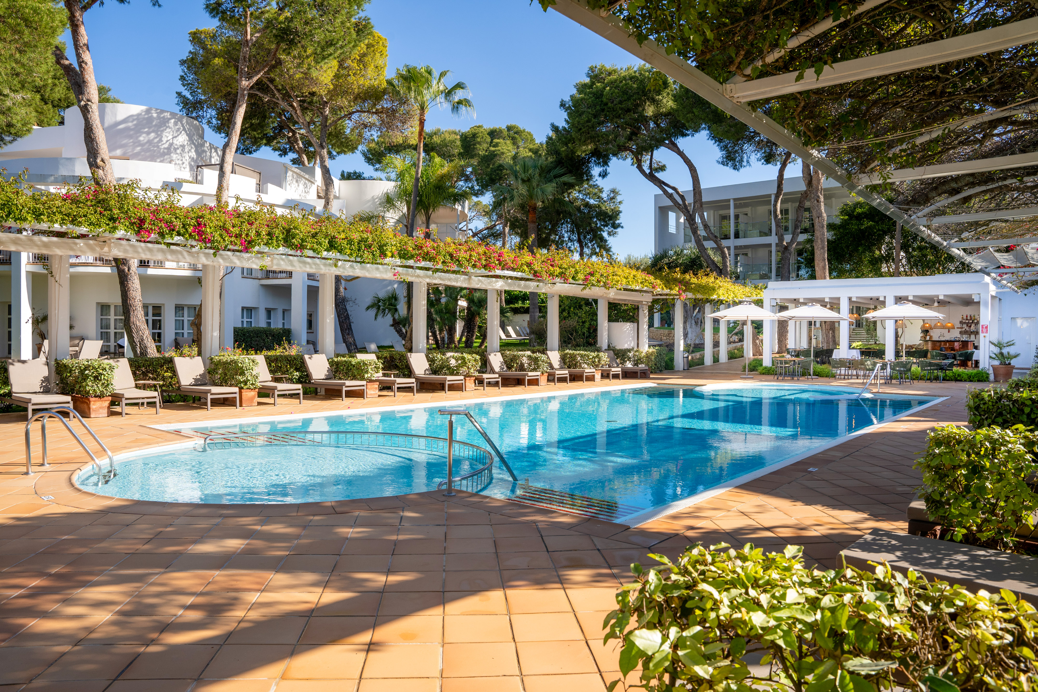 Sunny resort swimming pool with lounge chairs, white buildings, and lush greenery. - Piscine paesaggistiche sorprendenti - Meliá Cala d'Or Boutique Hotel, Maiorca