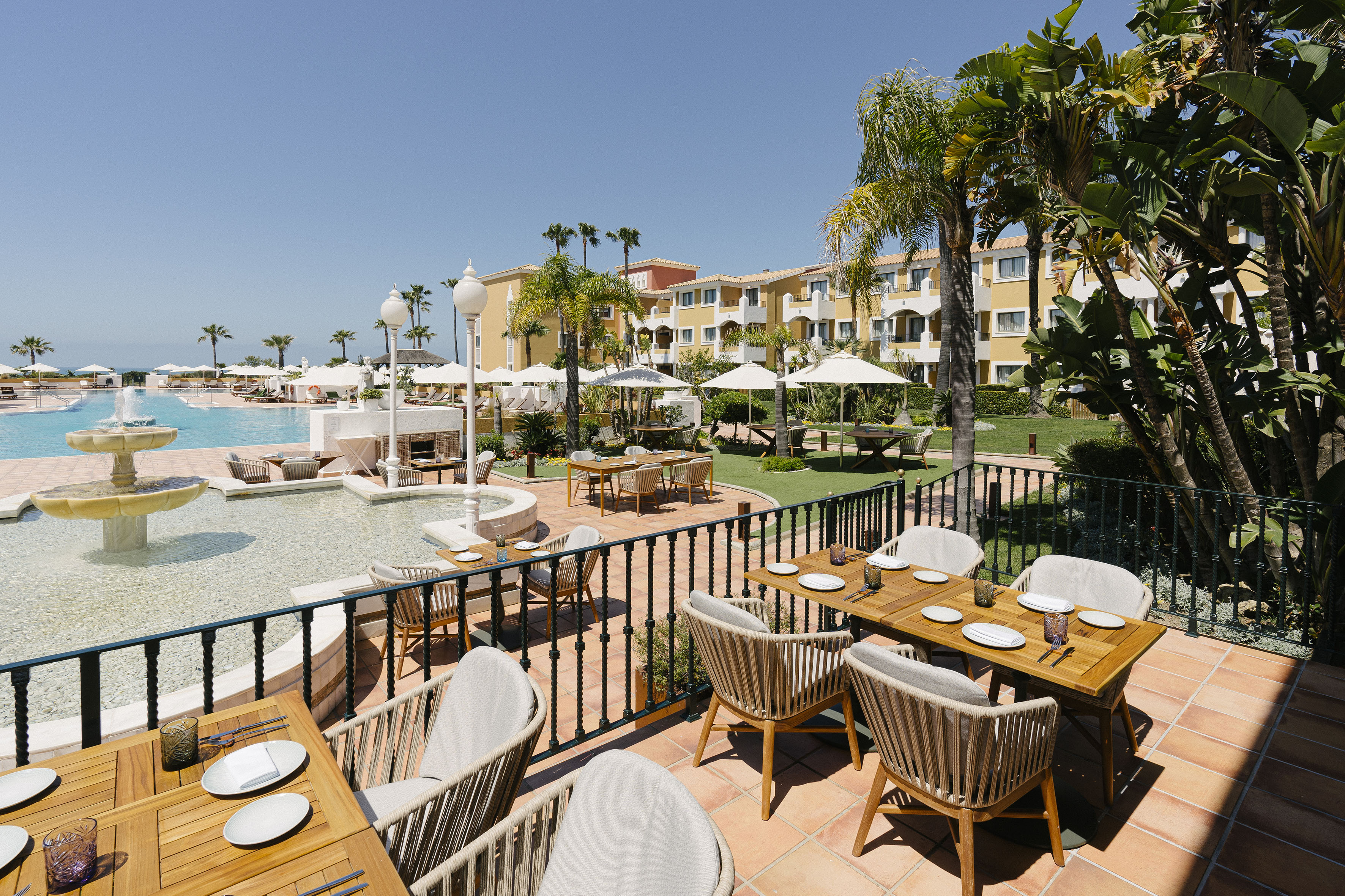 Luxury resort outdoor dining terrace with set tables, pool, and palm trees.