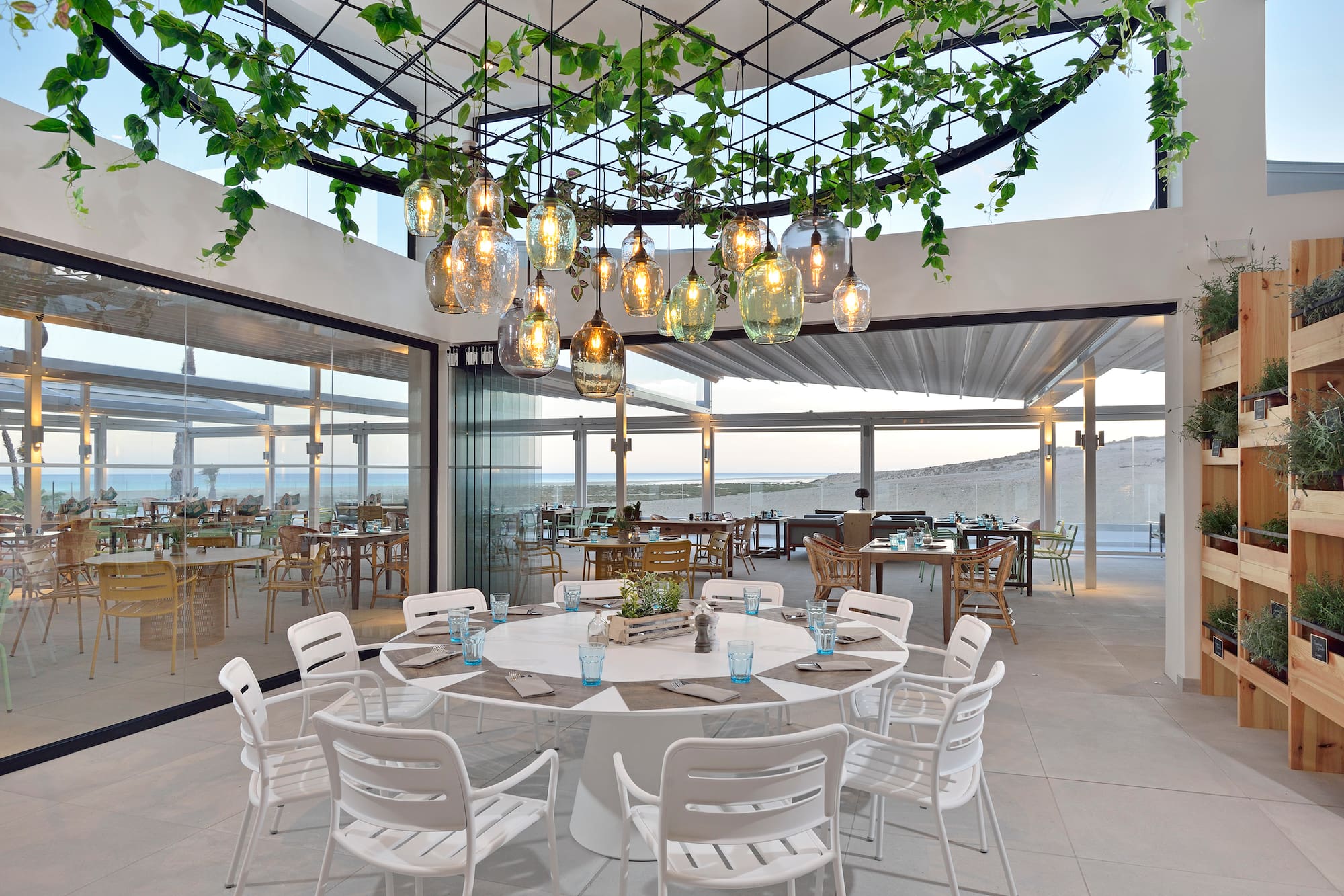 Coastal restaurant with panoramic ocean view, modern decor, and hanging plants.
