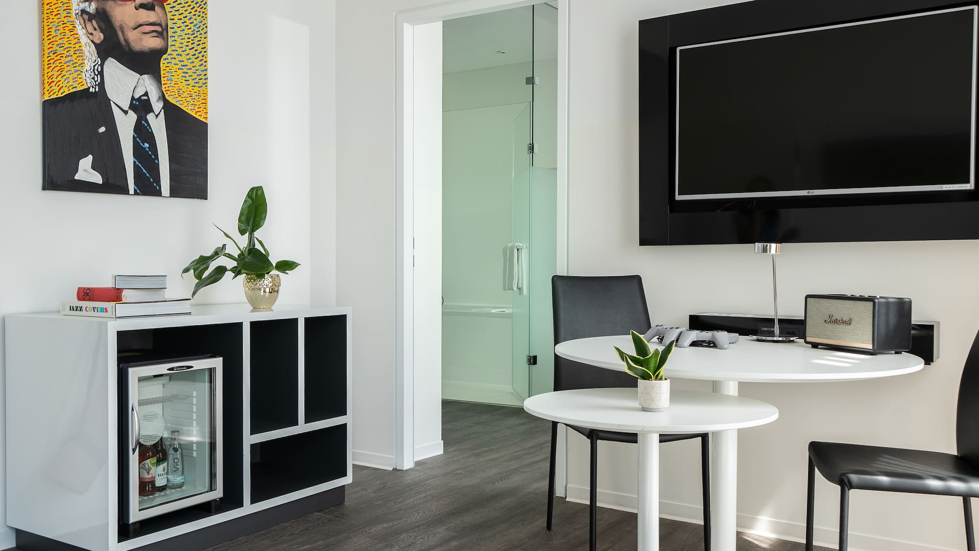 Modern hotel room with Karl Lagerfeld art, TV, mini-fridge, and dining area.