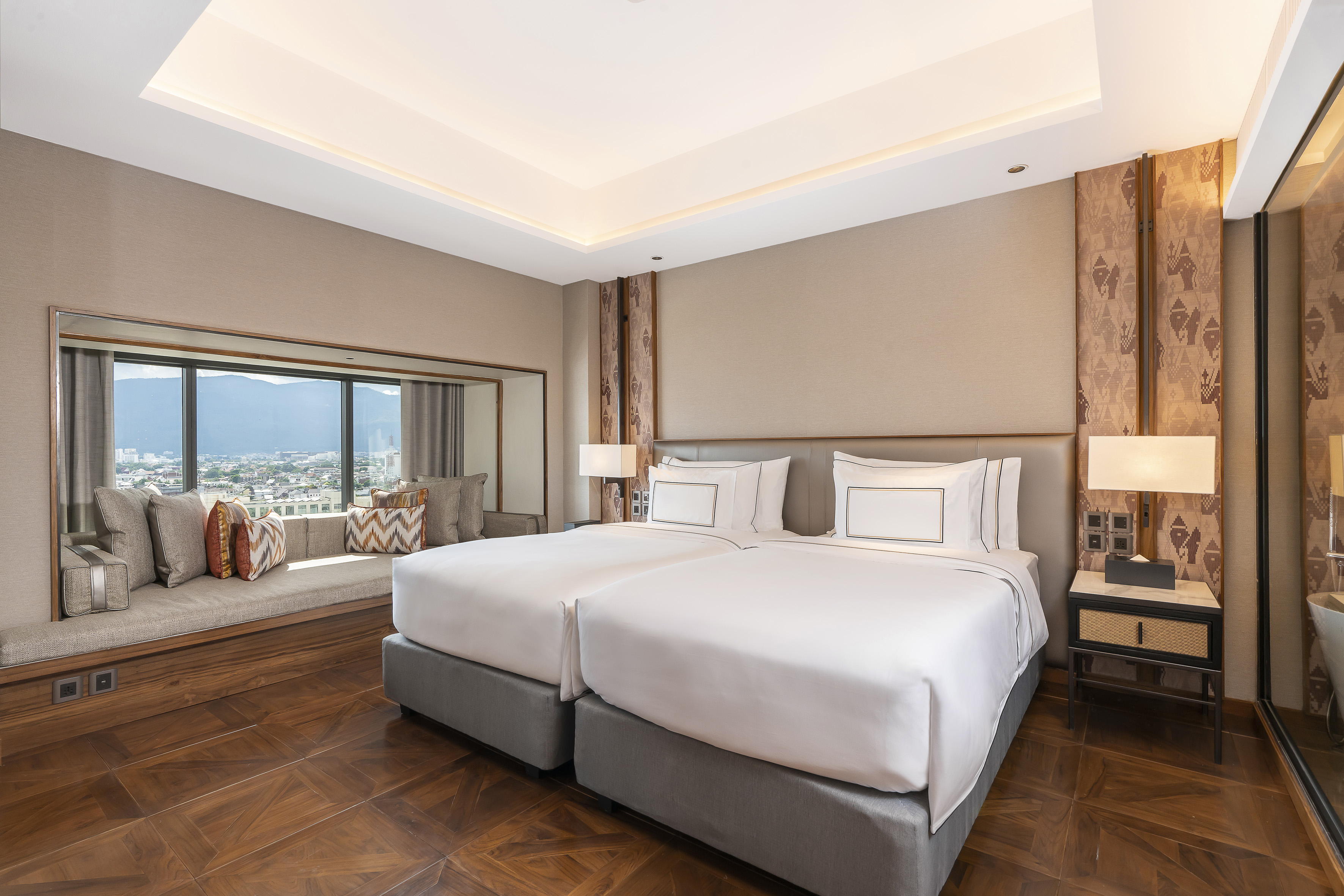 Luxury hotel room with twin beds, city view, and spacious window seat.