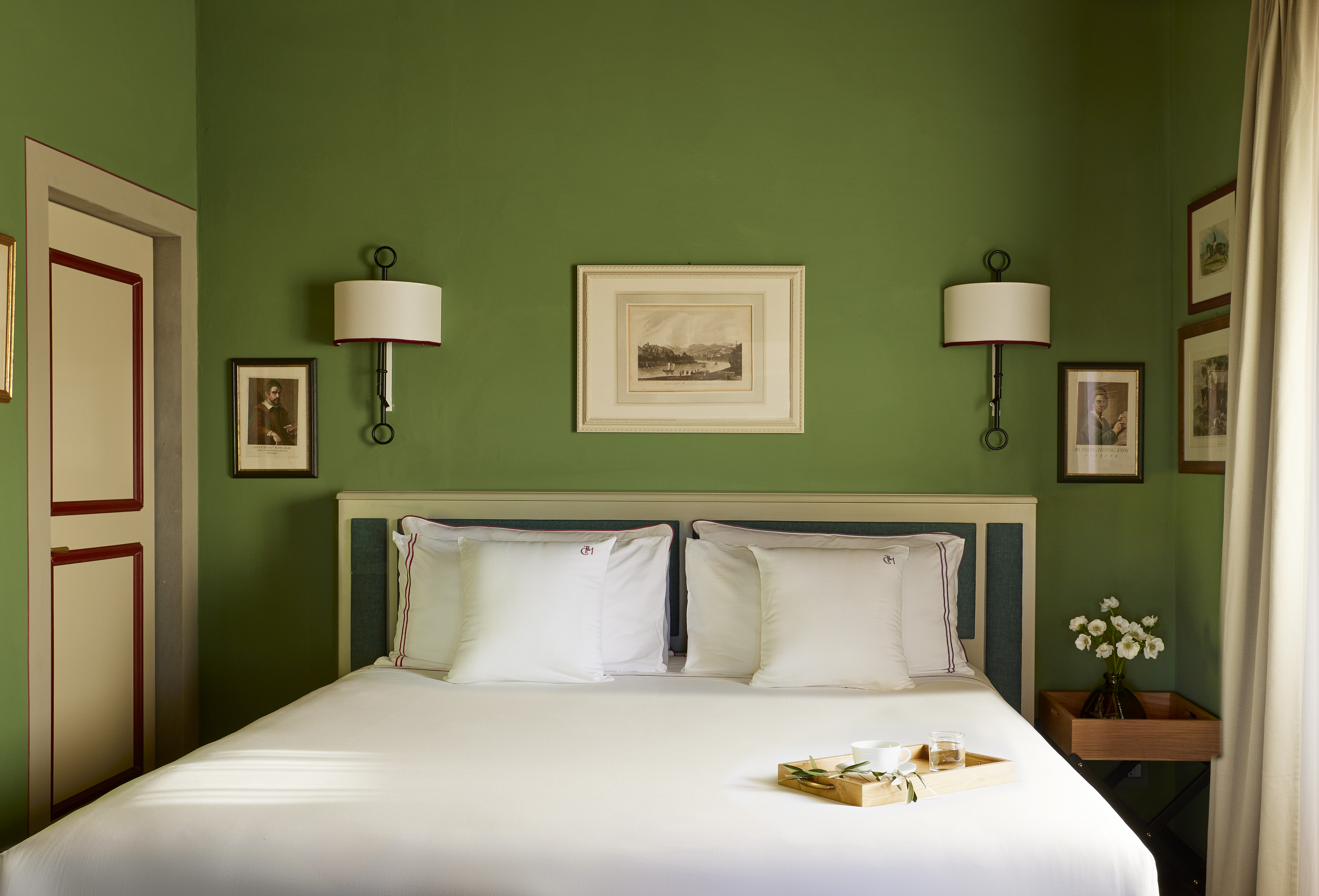 Vibrant green bedroom with white bed, framed art, and wall sconces.