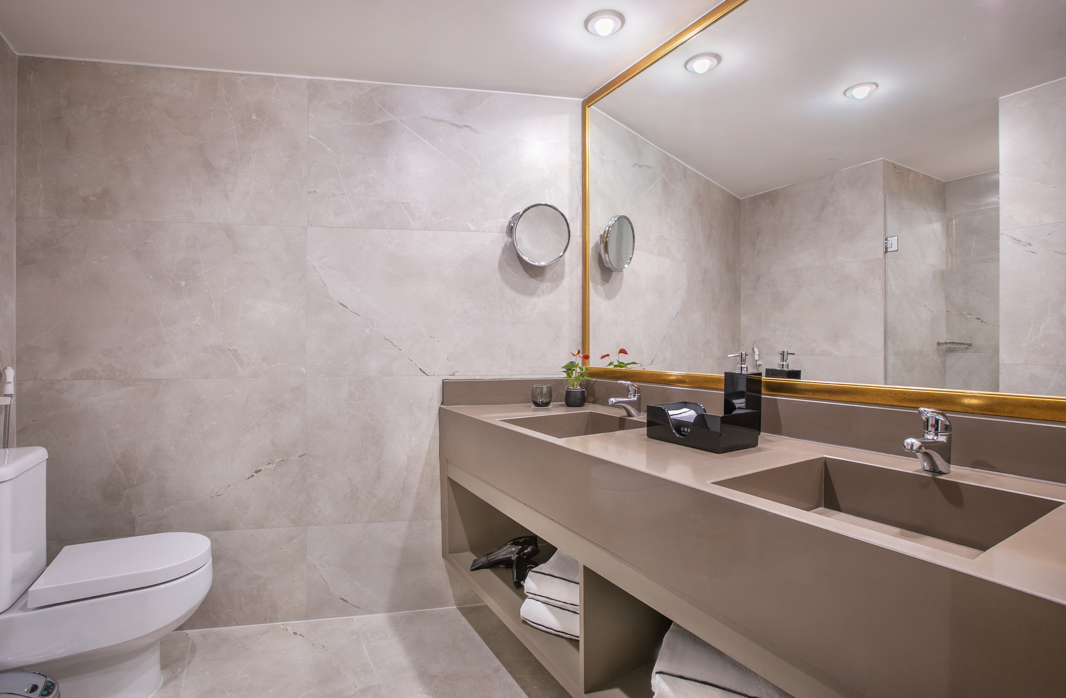 Contemporary bathroom with double vanity, gold mirror, and light marble walls.