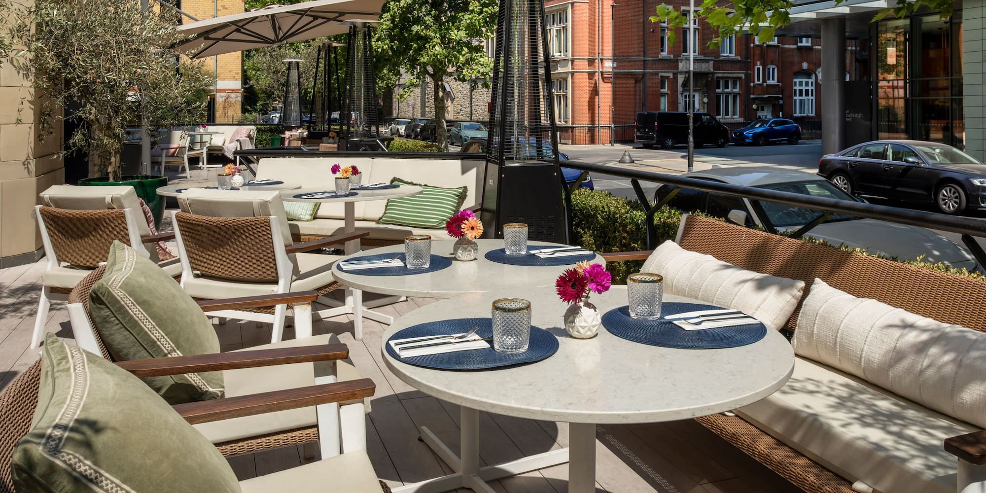 Outdoor restaurant terrace with tables, comfy seating, umbrellas & heaters.