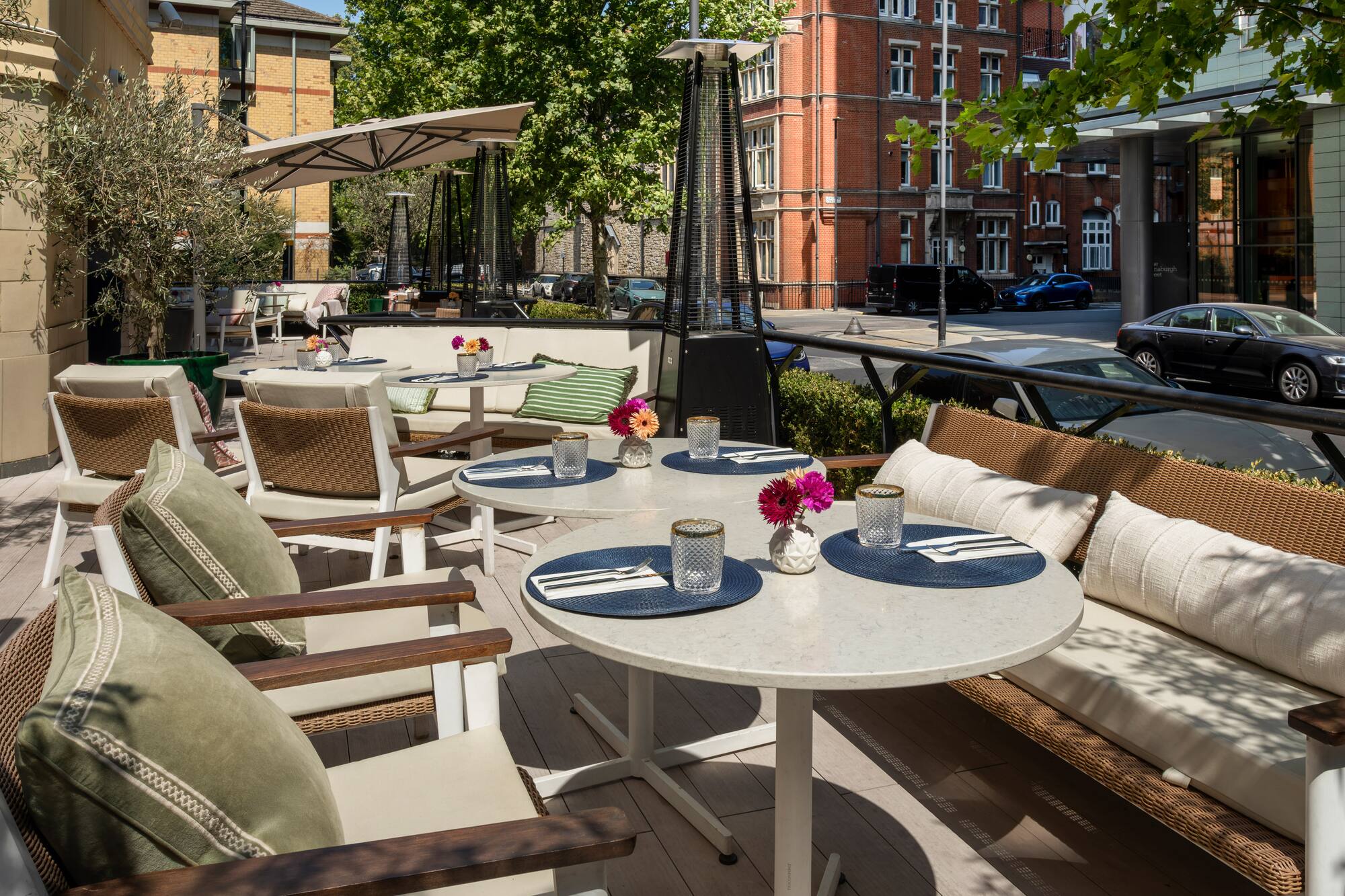Outdoor restaurant terrace with tables, comfy seating, umbrellas & heaters.