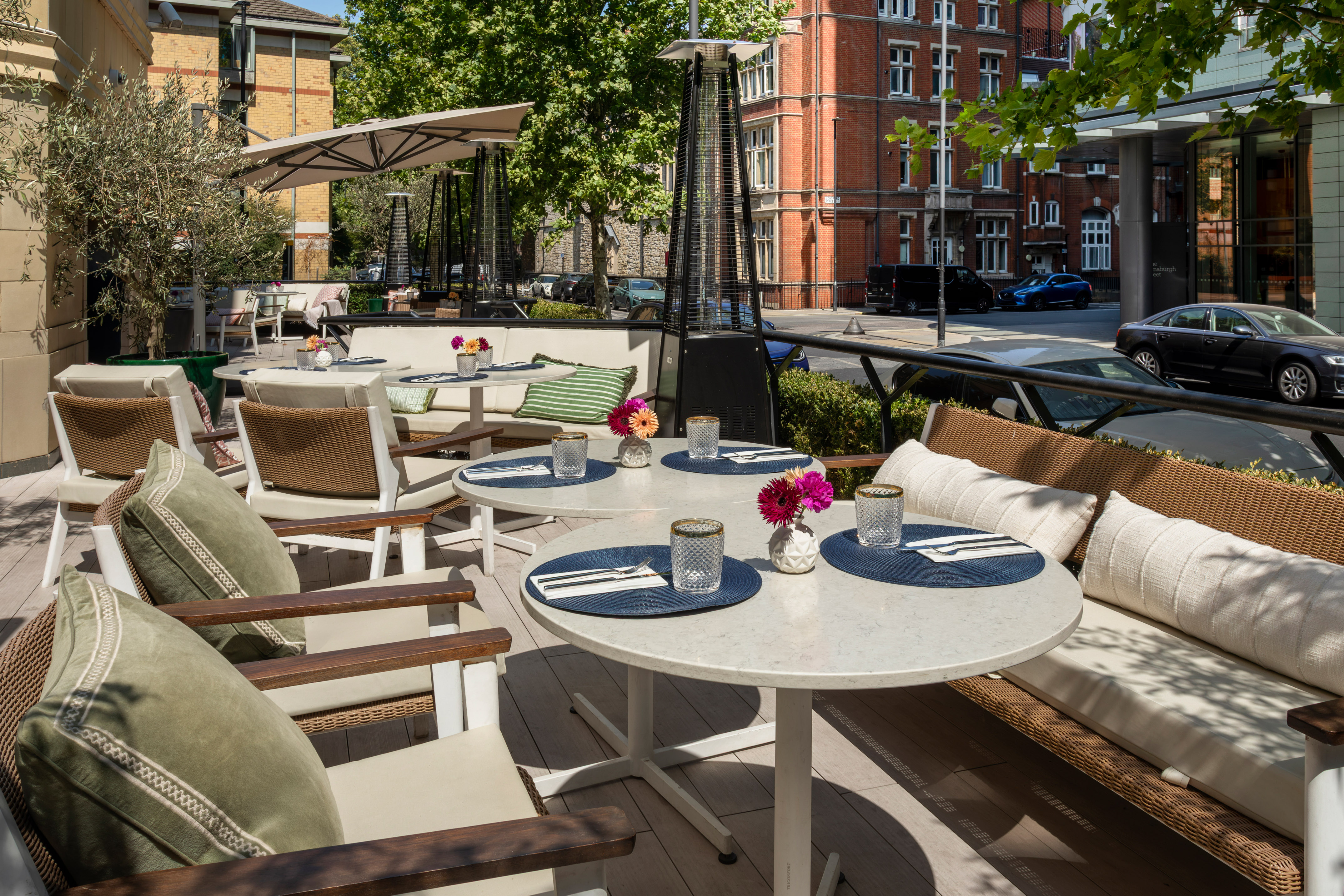 Outdoor restaurant terrace with tables, comfy seating, umbrellas & heaters.