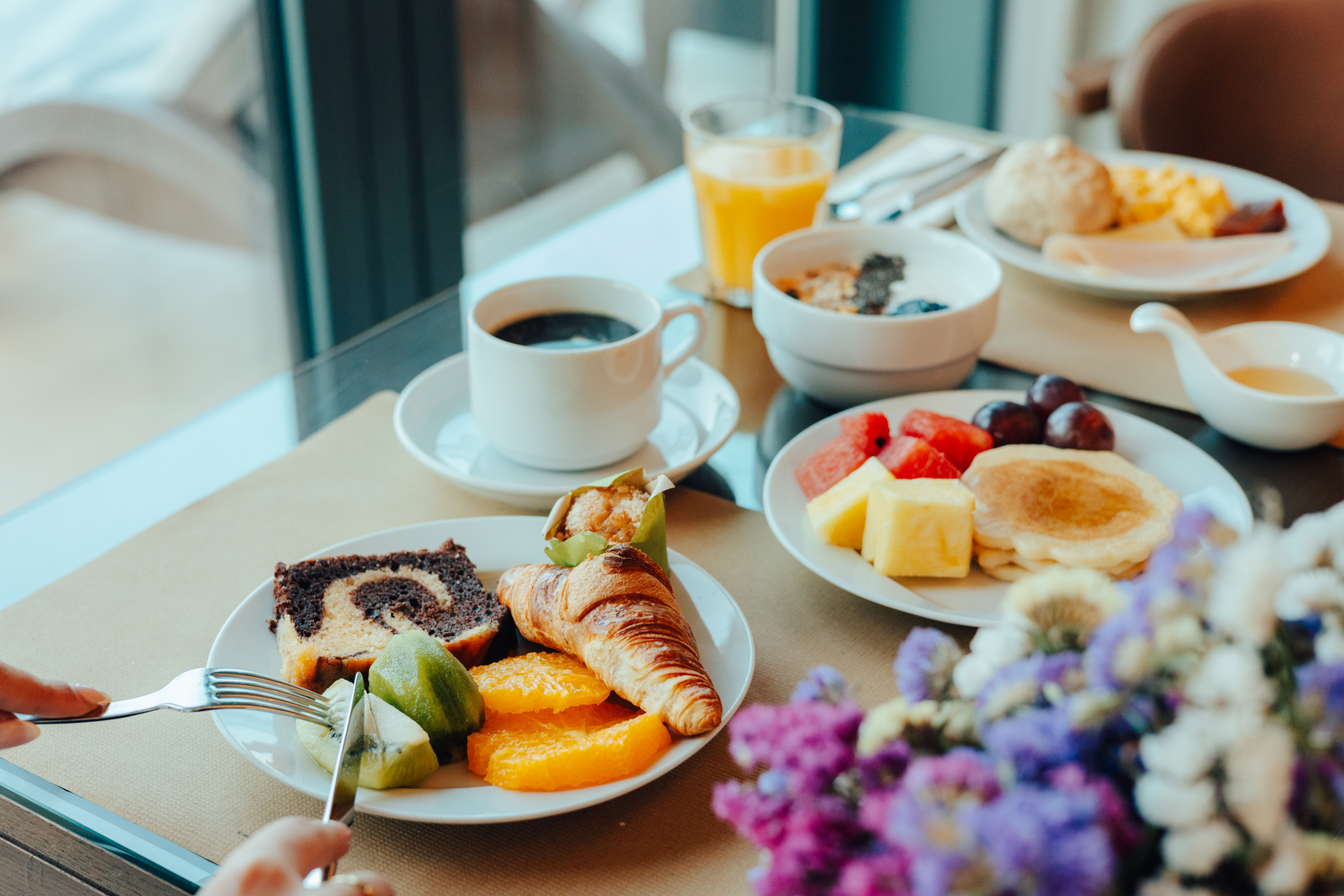 Full breakfast with coffee, croissant, fruit, pancakes, and scrambled eggs.