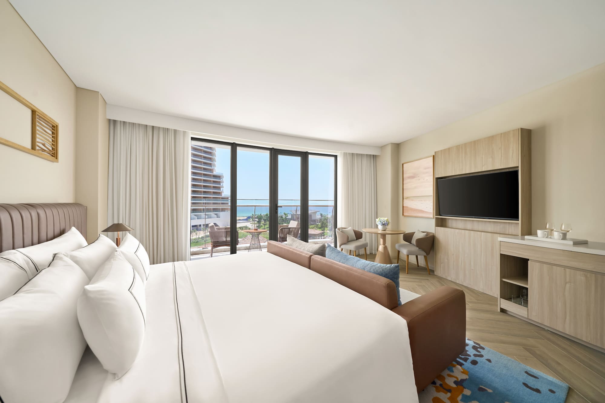 Modern luxury hotel room with ocean view balcony, large bed, and sofa.